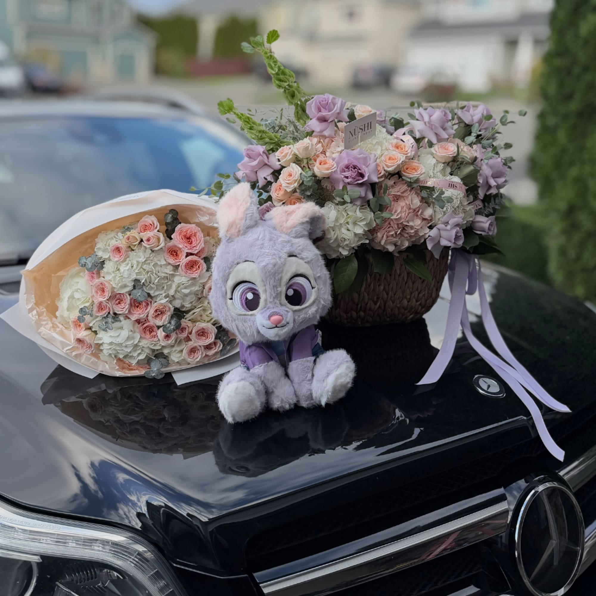 Two pastel flower arrangements and a plush bunny sit on a car hood