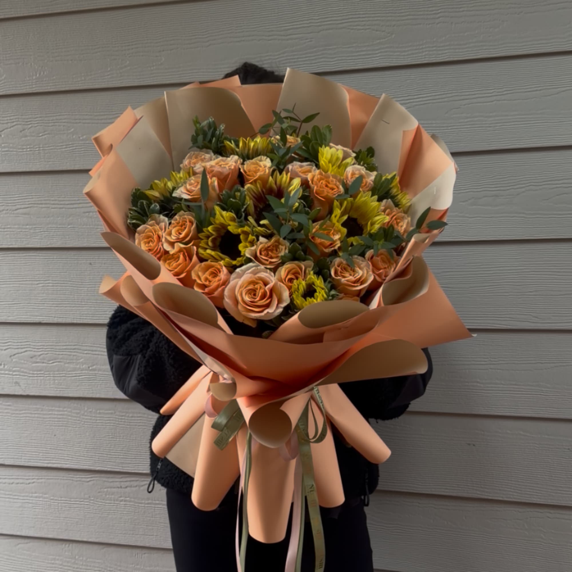 Large bouquet of peach roses and yellow sunflowers wrapped in peach paper