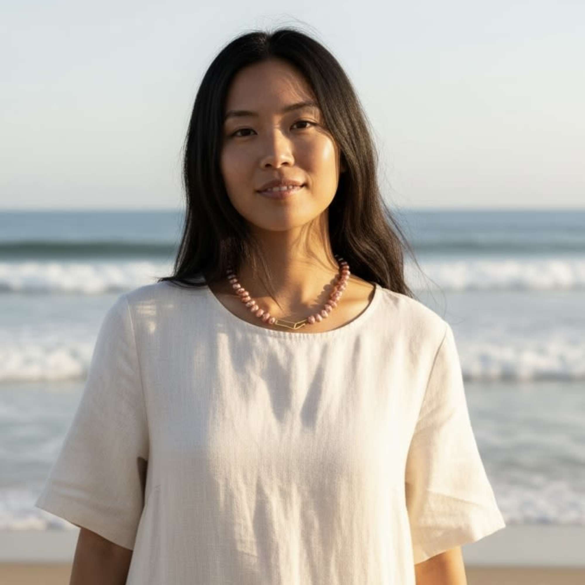 Woman standing on a beach wearing a light top and beaded necklace