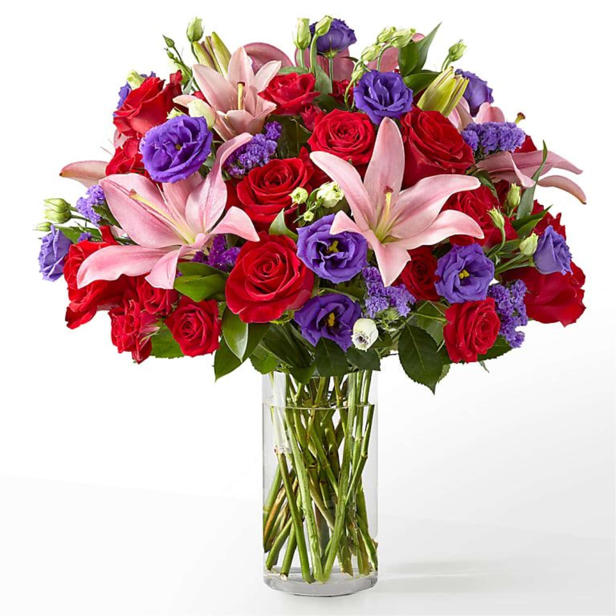 Bouquet of red roses, pink lilies, and purple blooms in a clear glass vase