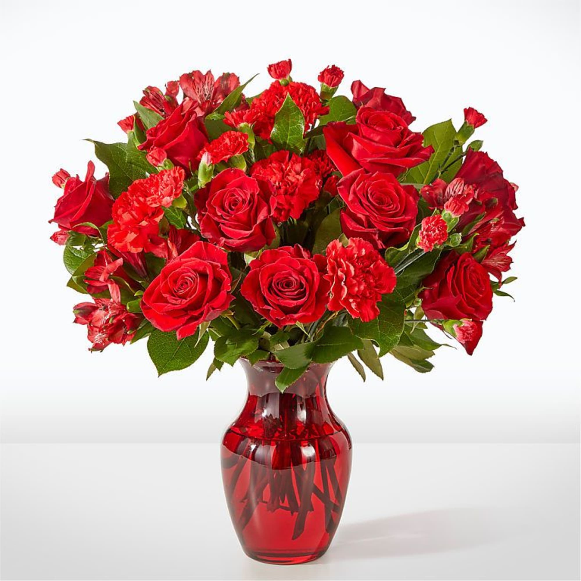Red roses and carnations arranged in a red glass vase