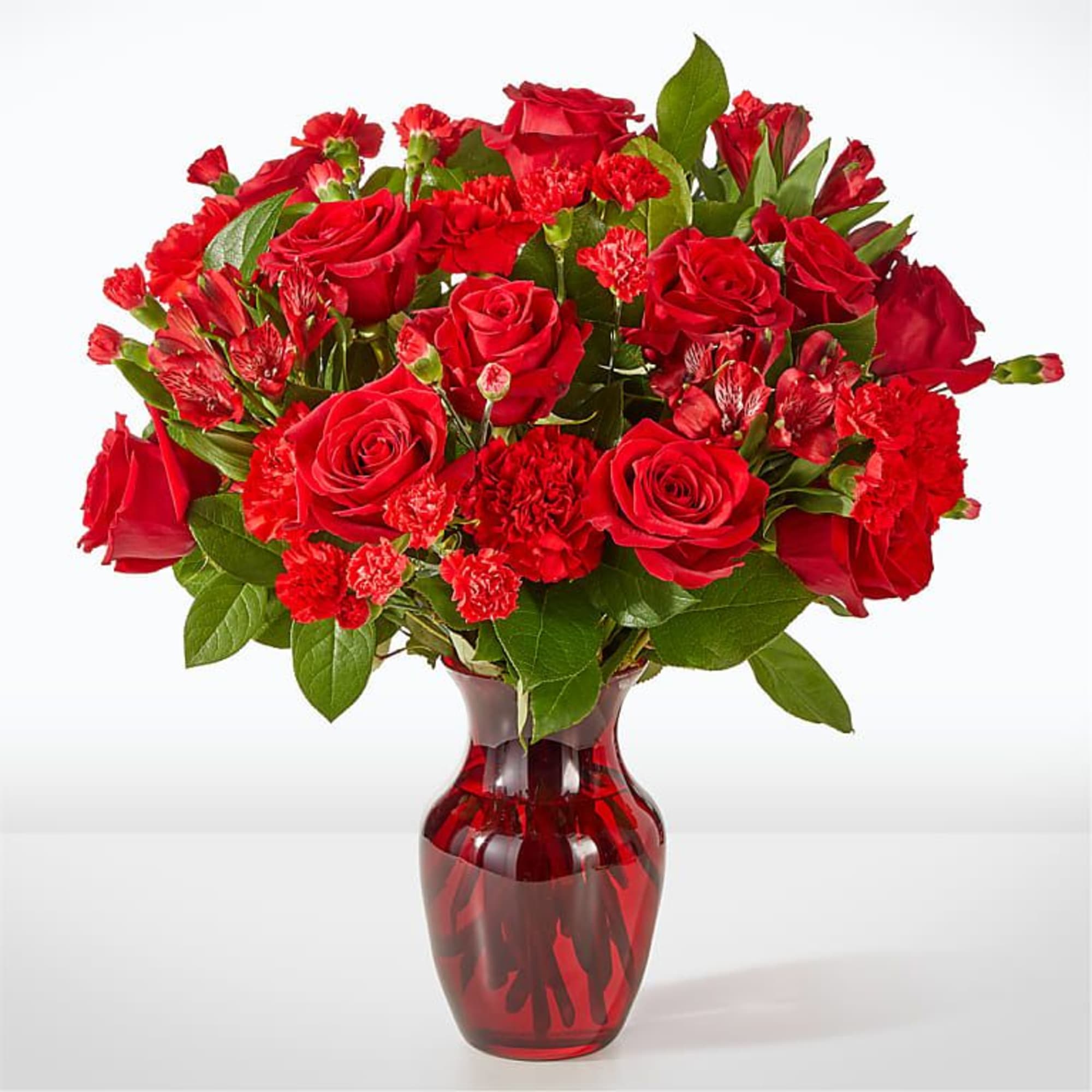 Red roses and carnations arranged in a red glass vase