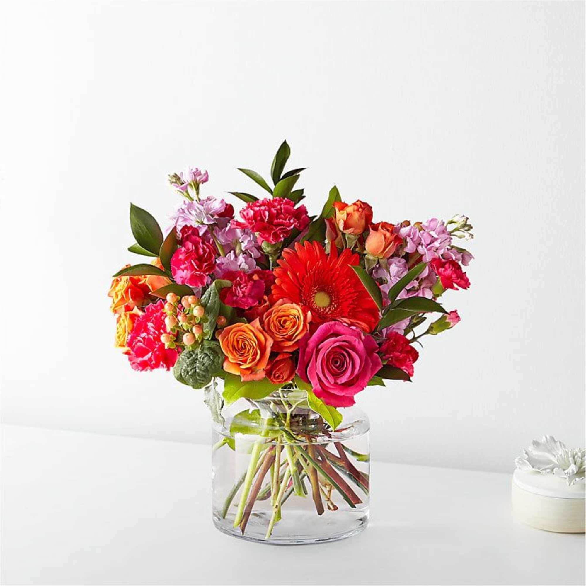 Mixed bouquet of pink, orange, and red flowers in a clear glass vase