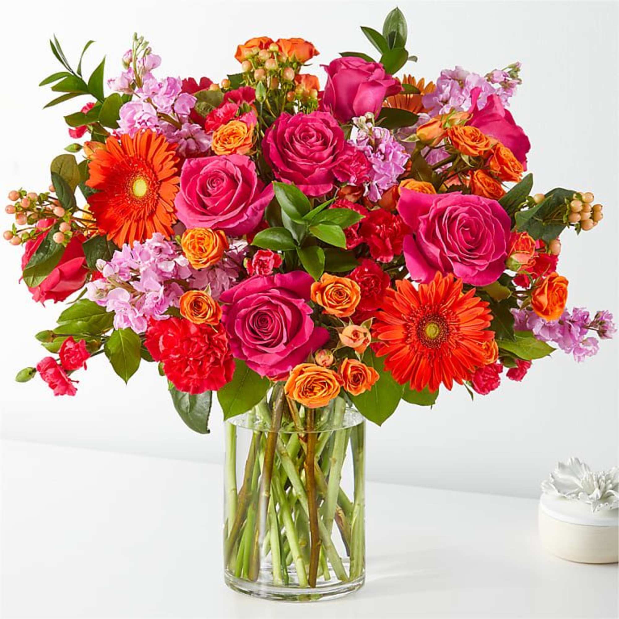 Bright mixed bouquet of roses, gerbera daisies, and lilac in a clear glass vase