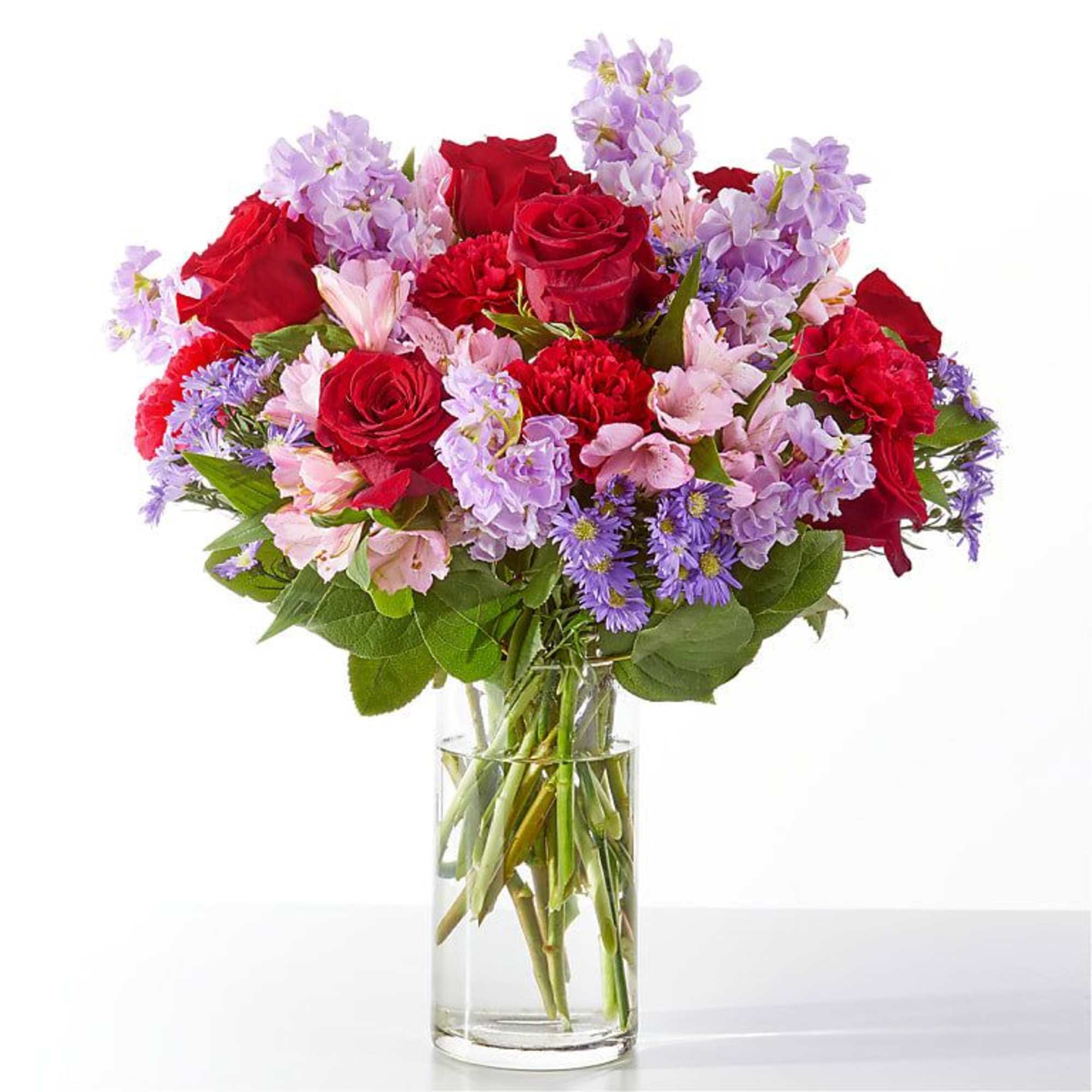 Bouquet of red roses, pink flowers, and purple blooms in a clear glass vase