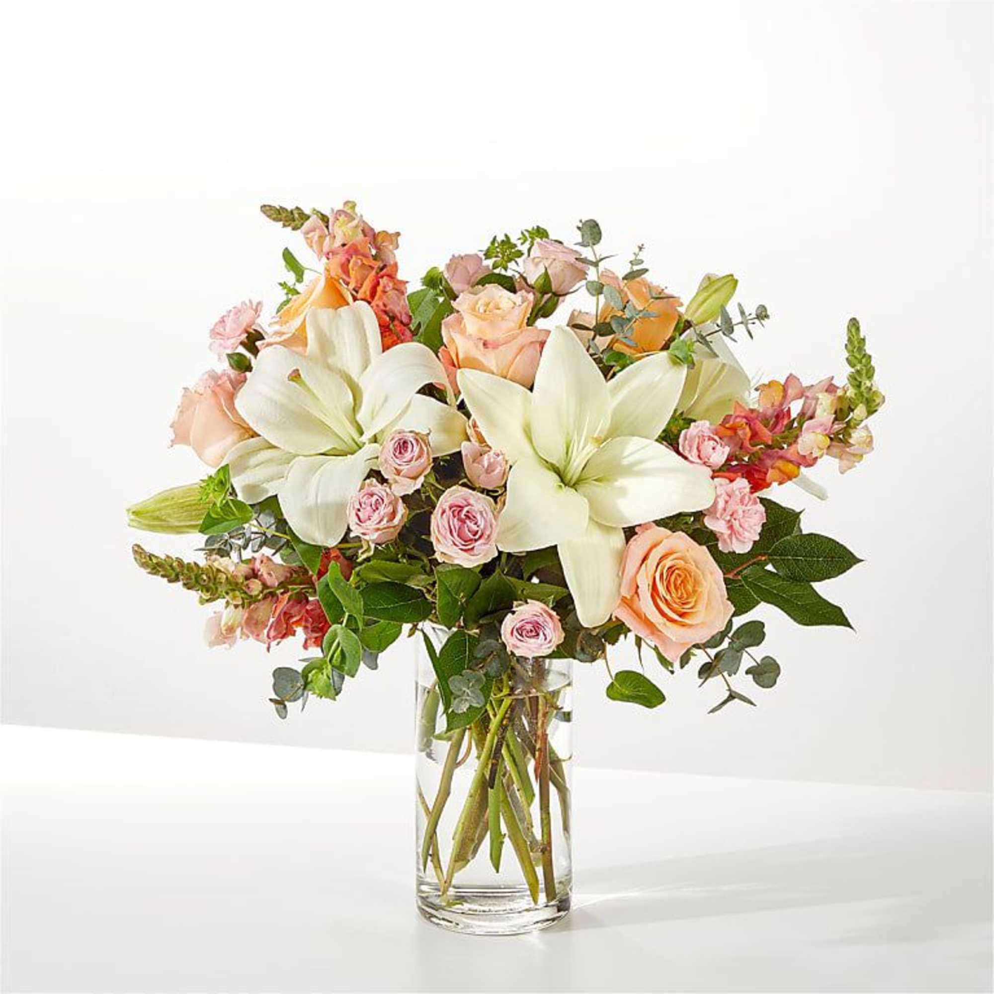 Bouquet of white lilies and peach roses in a clear glass vase