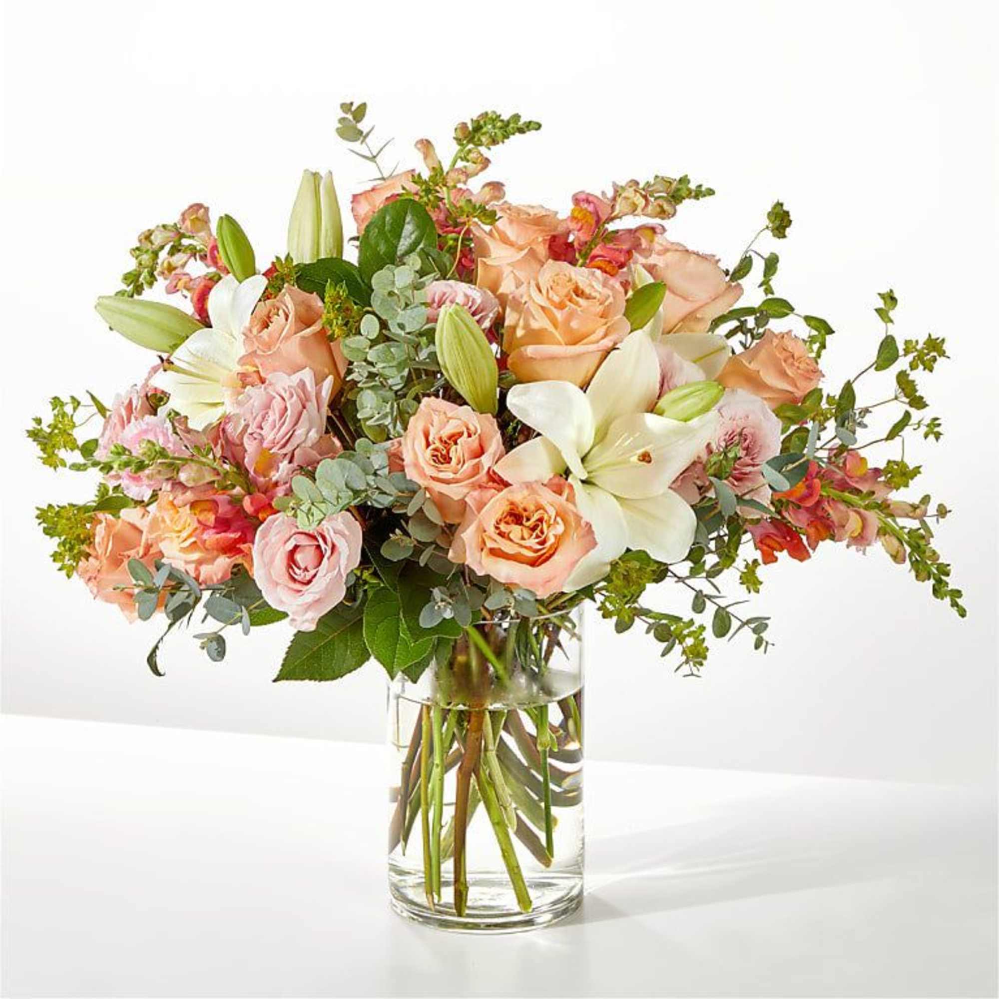 Peach and pink rose bouquet in a clear glass vase with white lilies