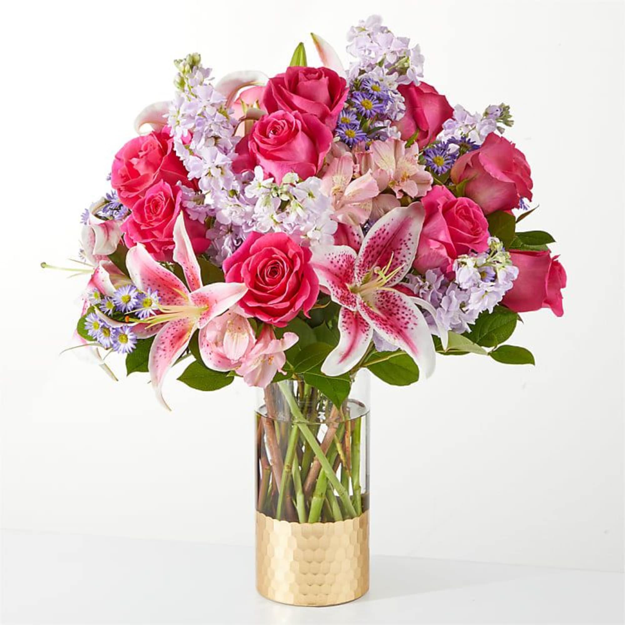 Pink roses and lilies arranged in a clear glass vase with a gold base