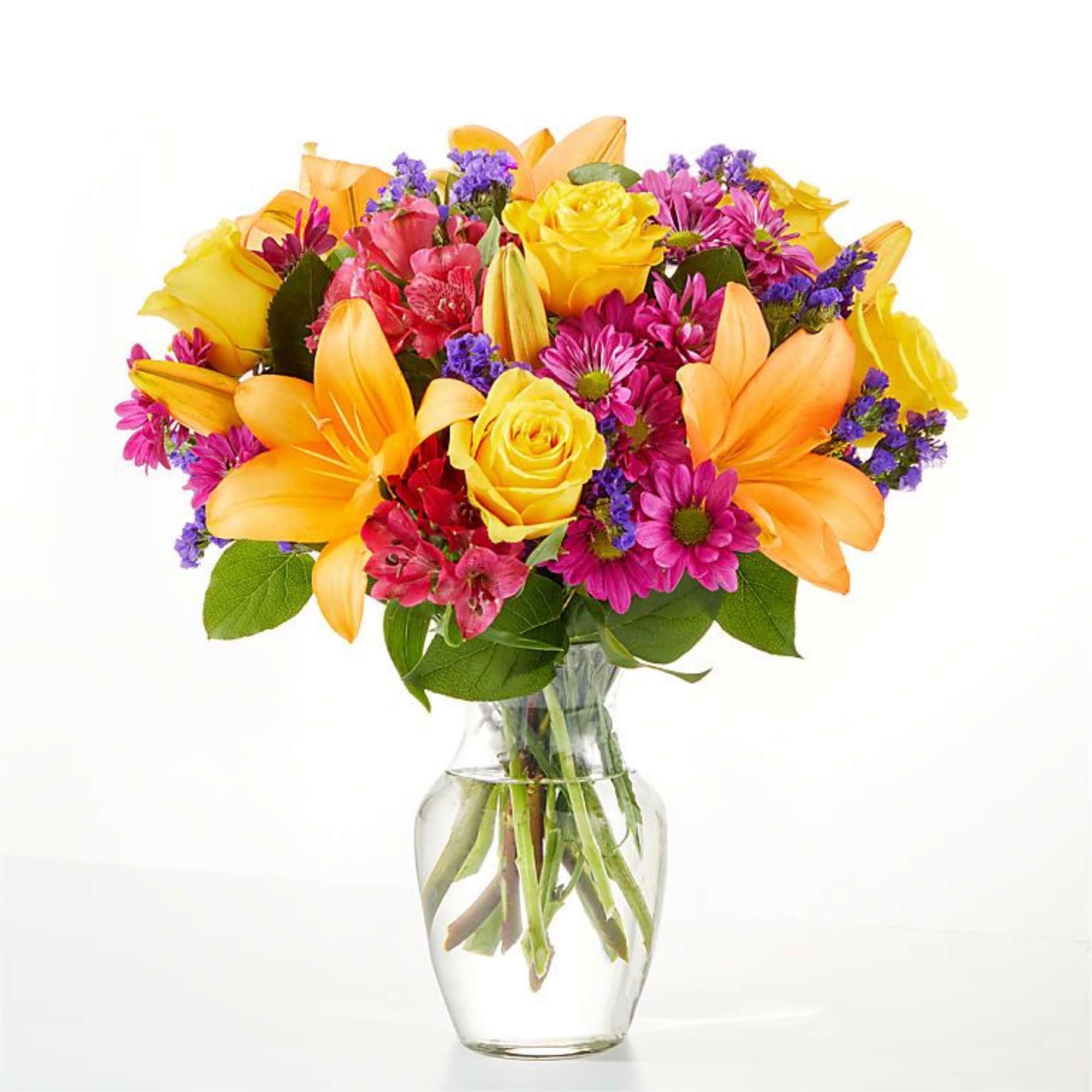 Bouquet of yellow roses, orange lilies, and pink daisies in a glass vase