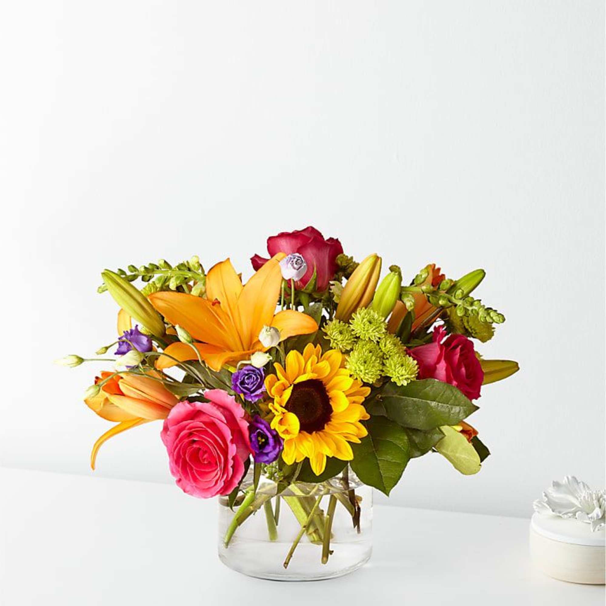 Mixed bouquet of roses, lilies, and a sunflower in a glass vase