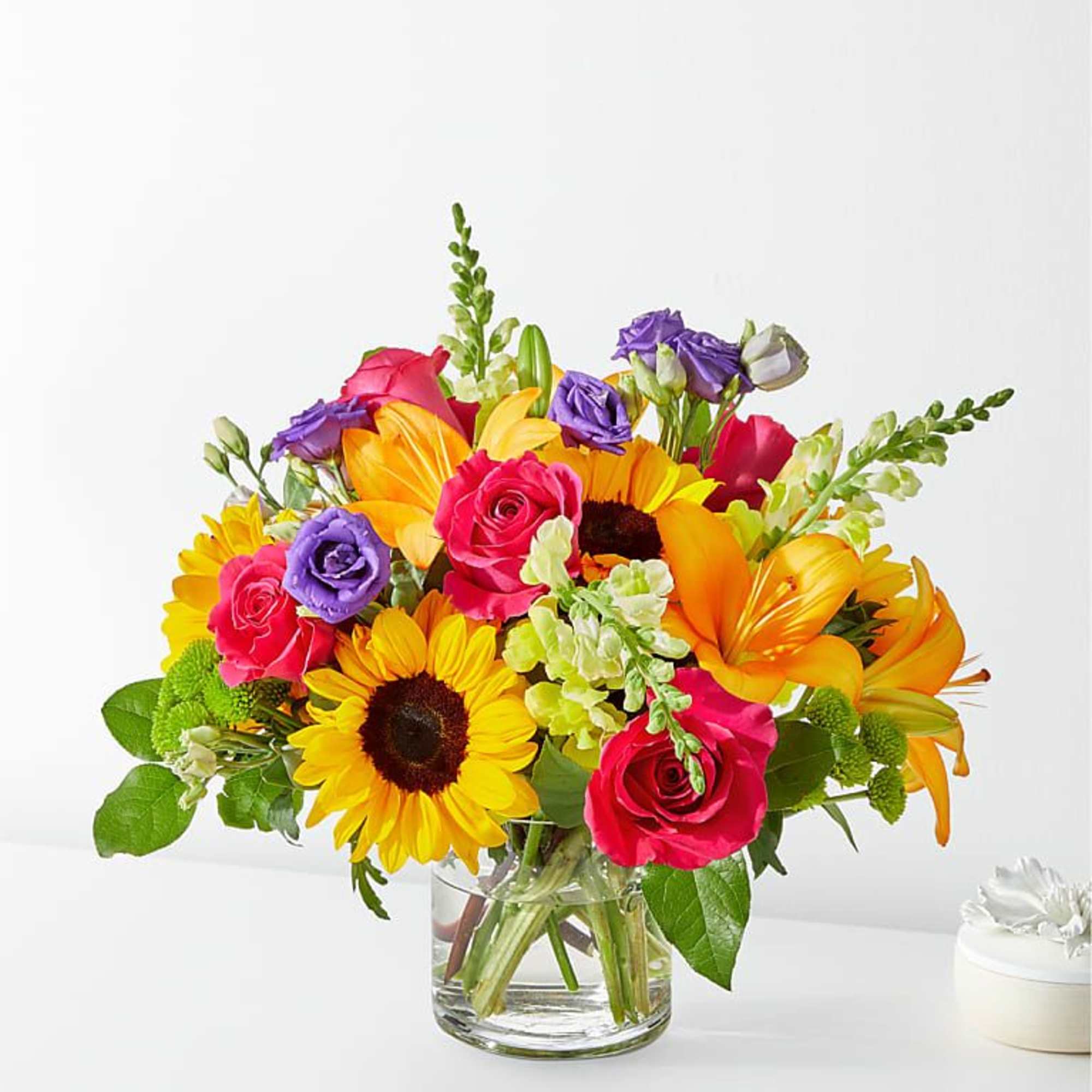 Bright mixed bouquet of sunflowers, roses, and lilies in a glass vase