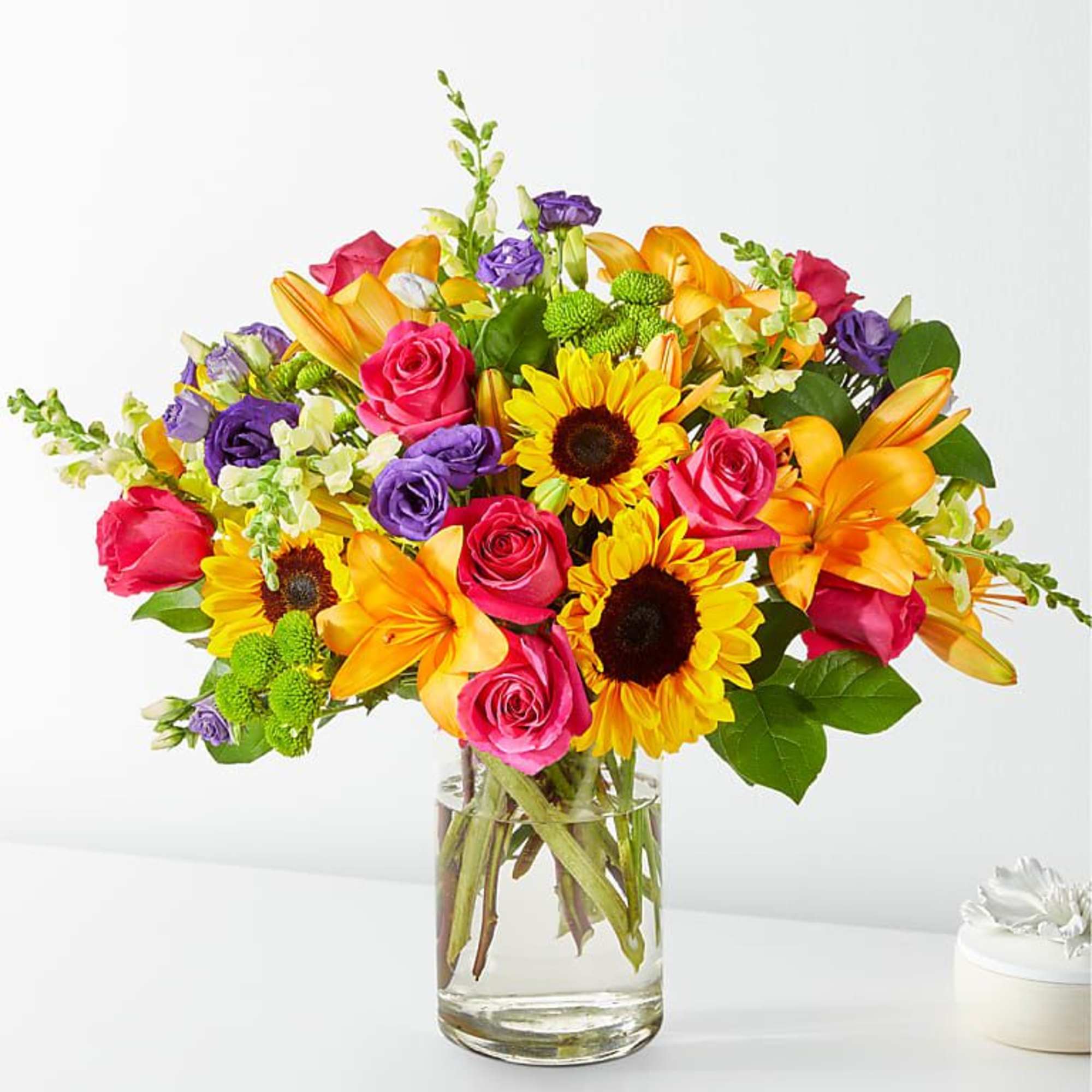 Bright mixed bouquet with roses, sunflowers, and lilies in a glass vase