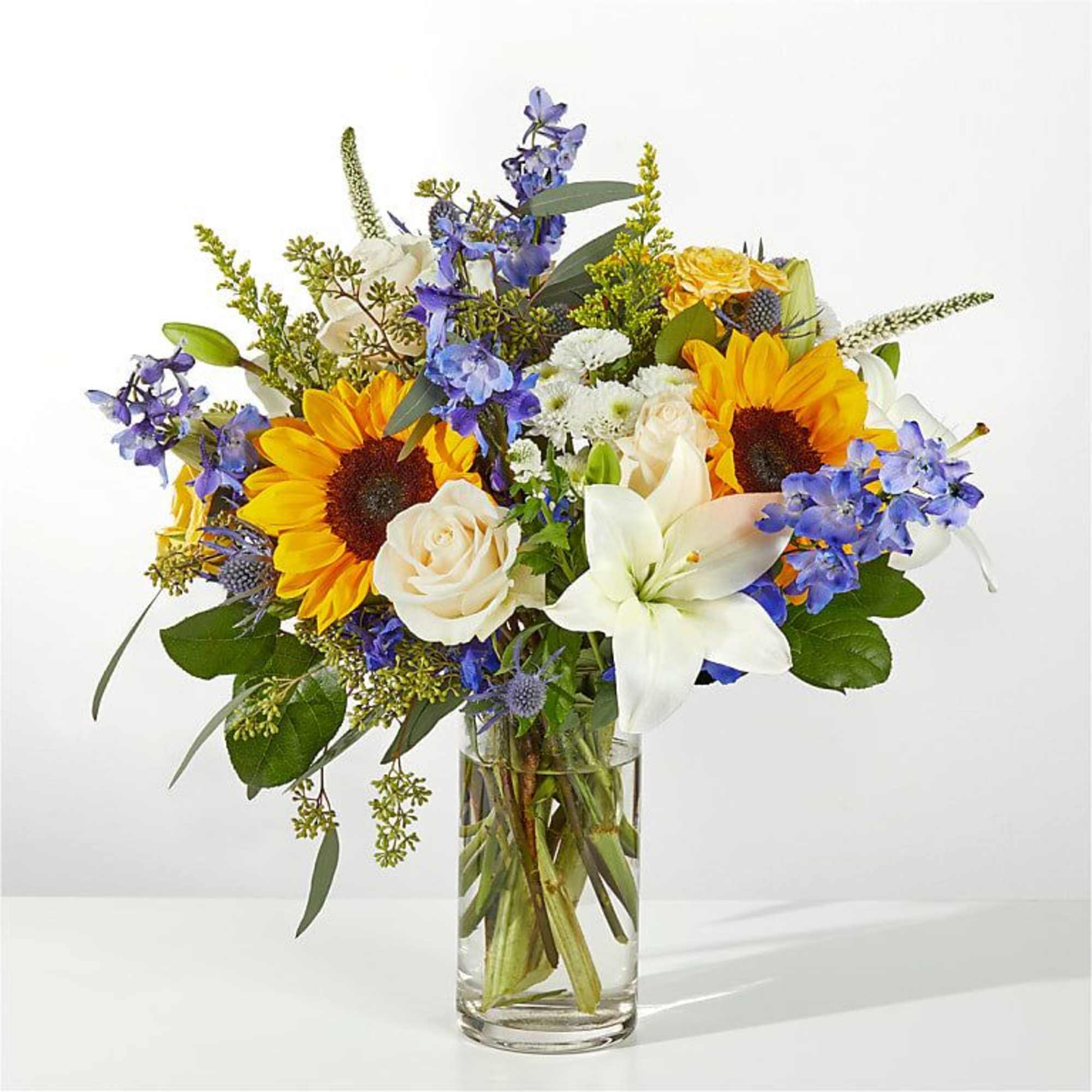 Bouquet of sunflowers, white lilies, and blue flowers in a glass vase