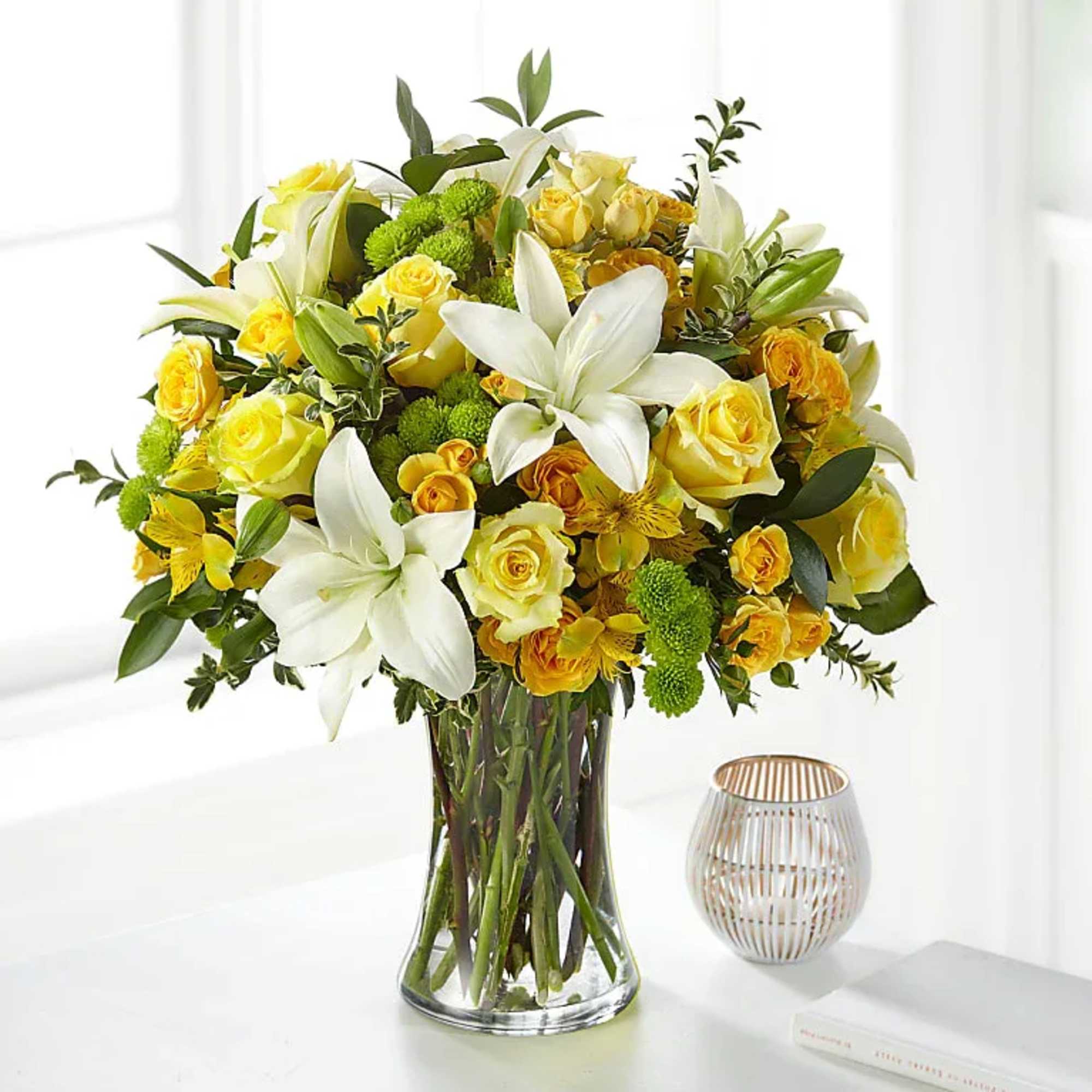 Yellow roses and white lilies arranged in a clear glass vase