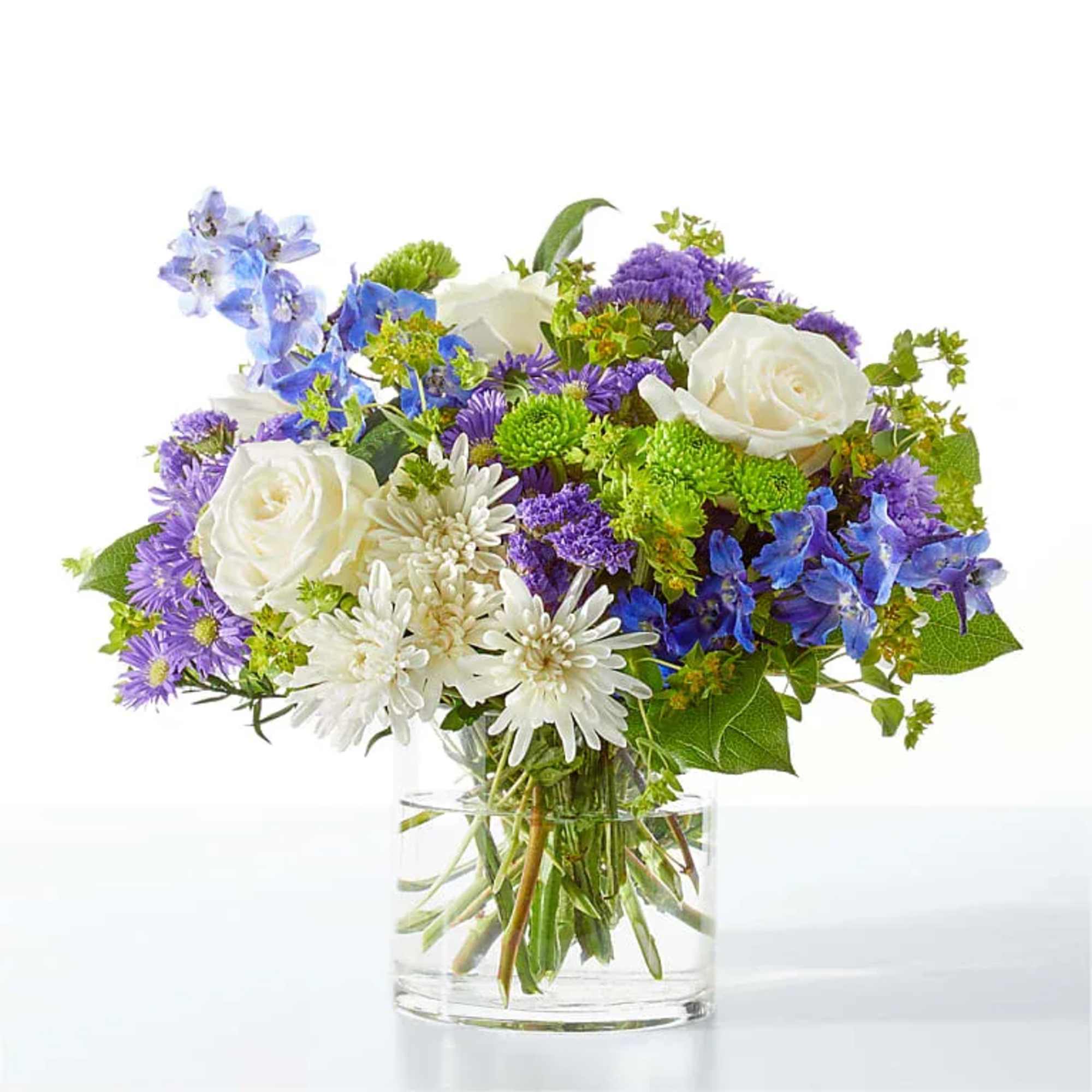 Bouquet of white roses, purple flowers, and blue blooms in a clear glass vase