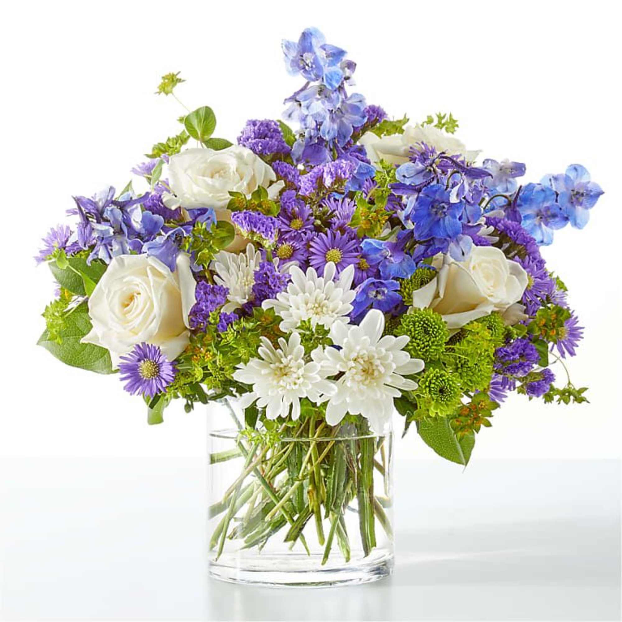 Bouquet of white roses, purple blooms, and blue flowers in a clear glass vase