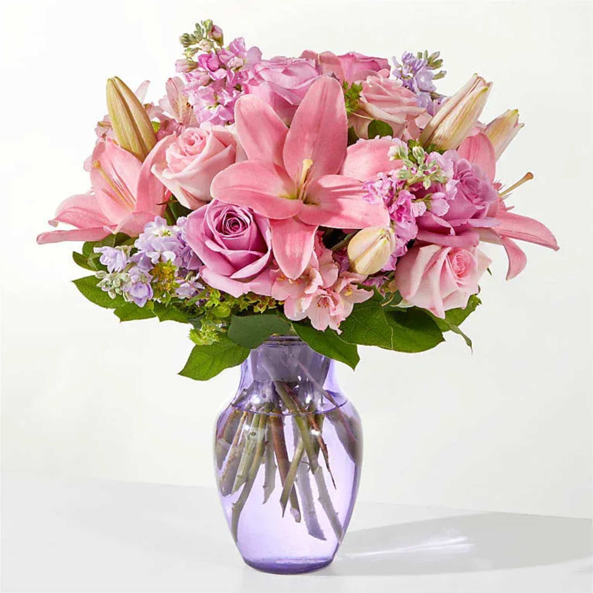 Pink lilies and roses arranged in a purple glass vase
