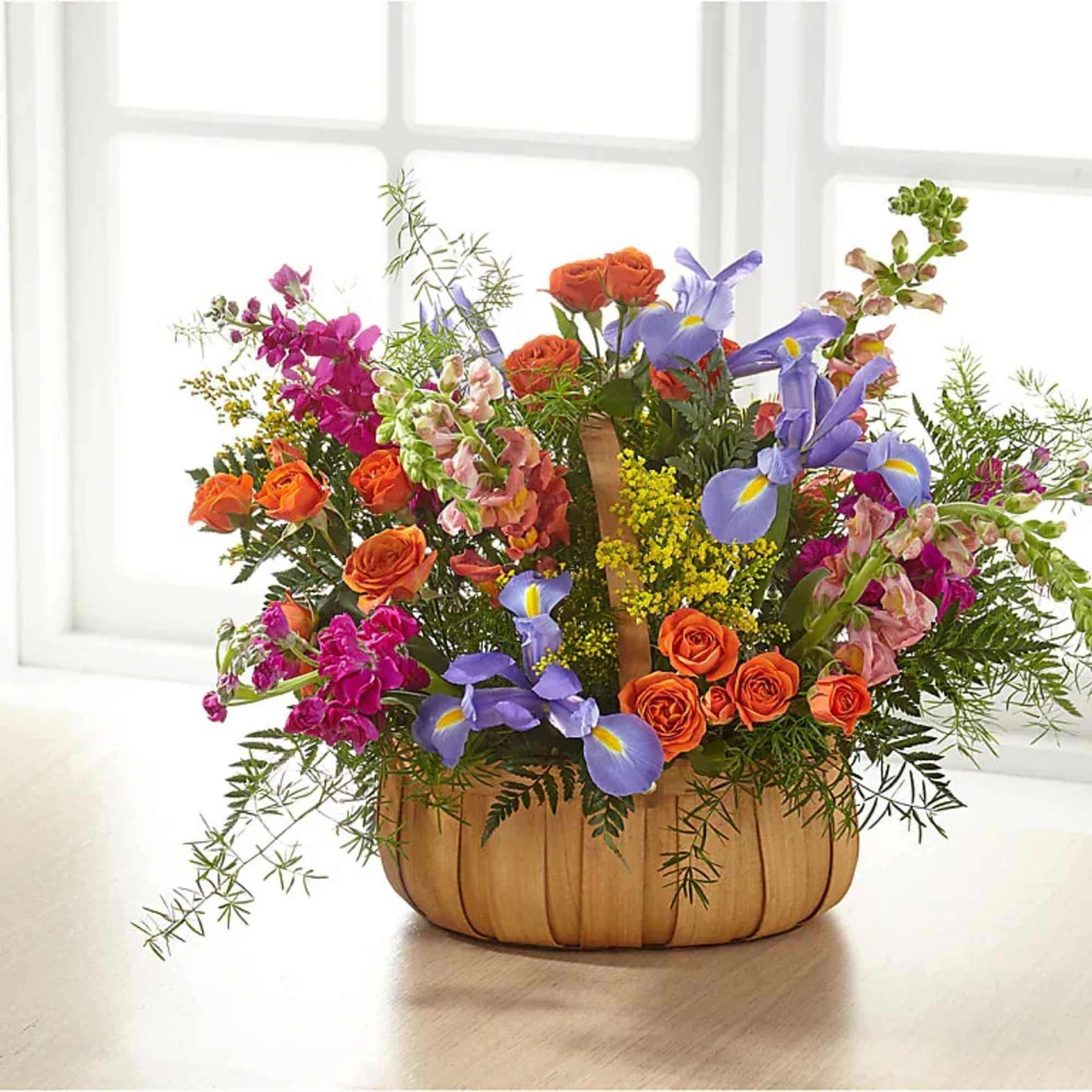 Basket arrangement of orange roses, purple irises, and pink flowers