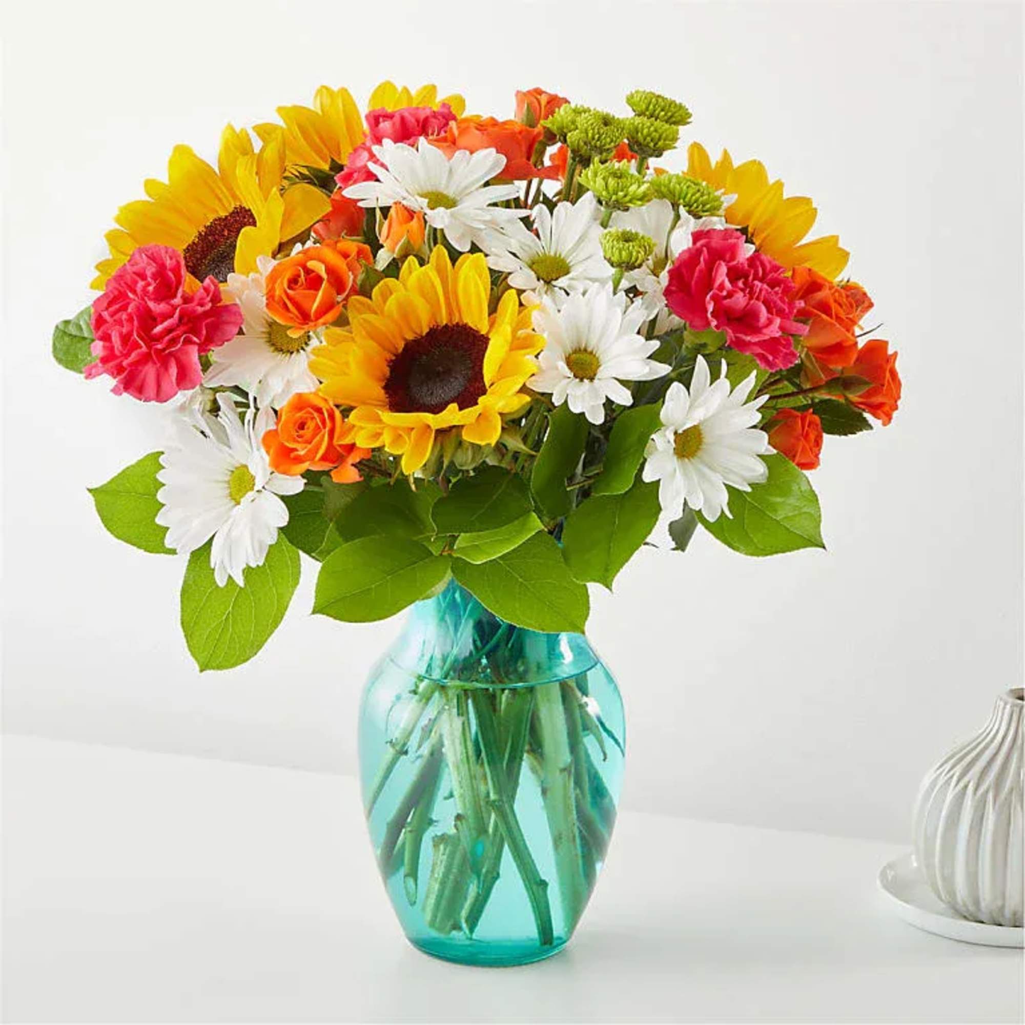Mixed bouquet of sunflowers, daisies, roses, and carnations in a blue glass vase