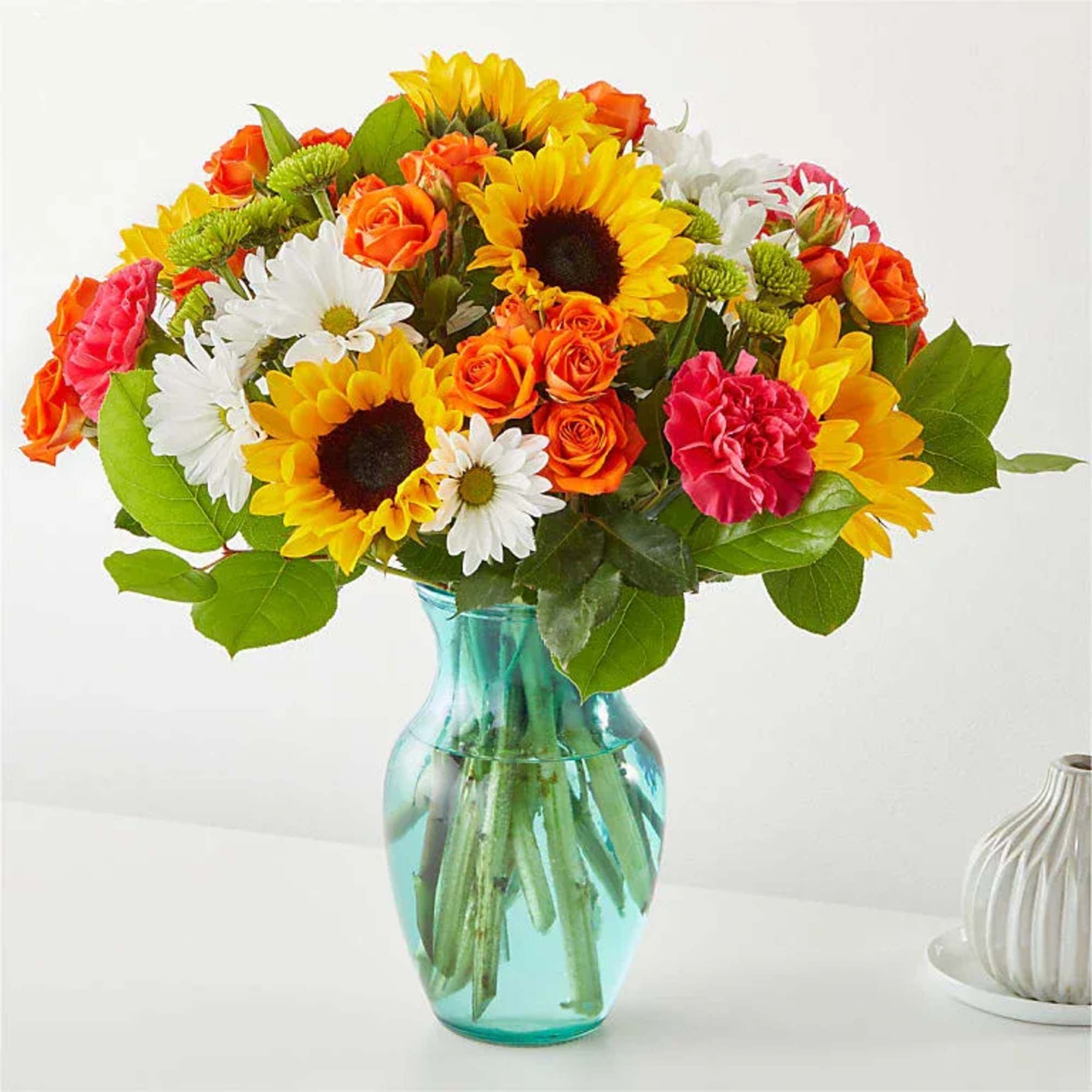 Mixed bouquet of sunflowers, roses, daisies, and carnations in a blue glass vase