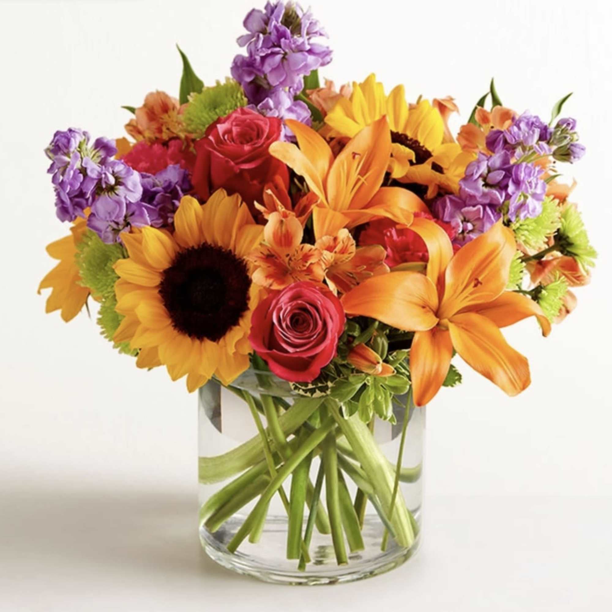 Colorful bouquet of sunflowers, roses, lilies, and purple blooms in a glass vase