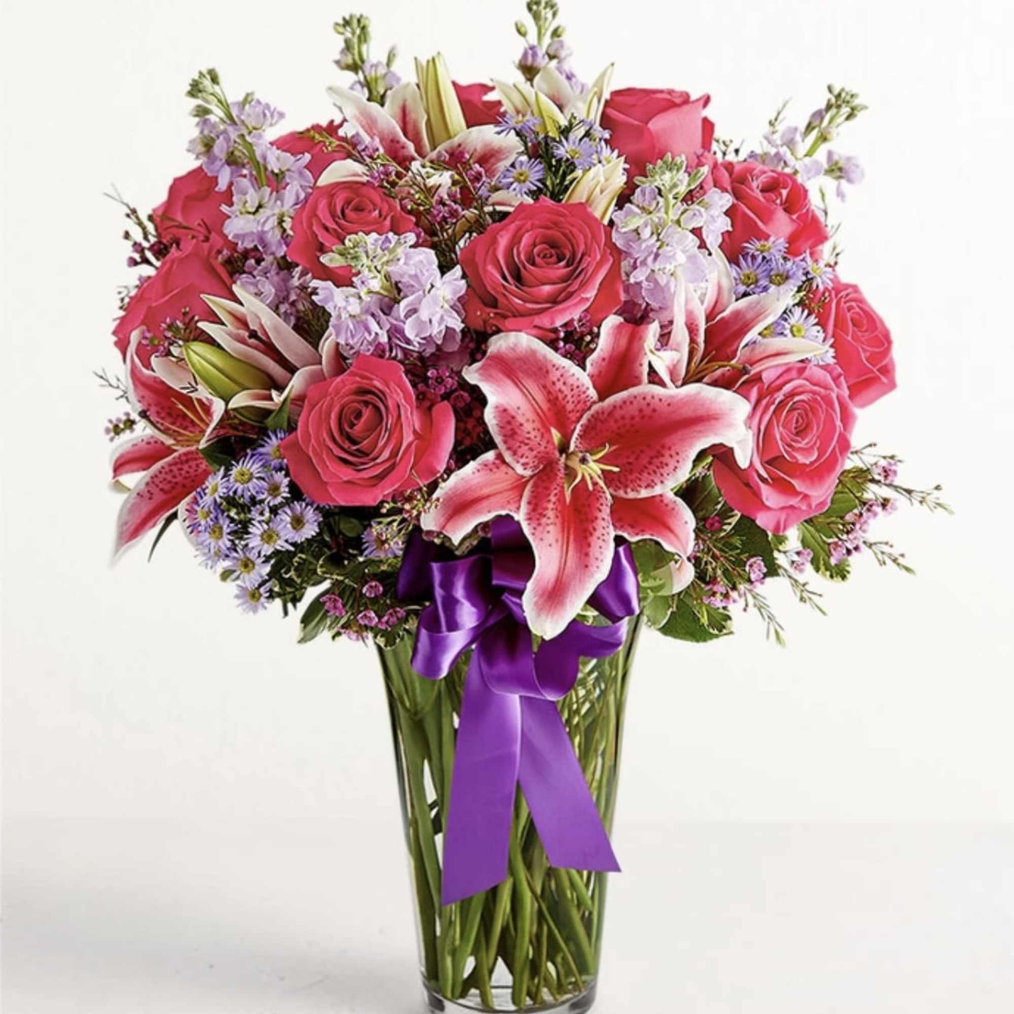 Pink roses and lilies in a clear glass vase with a purple ribbon