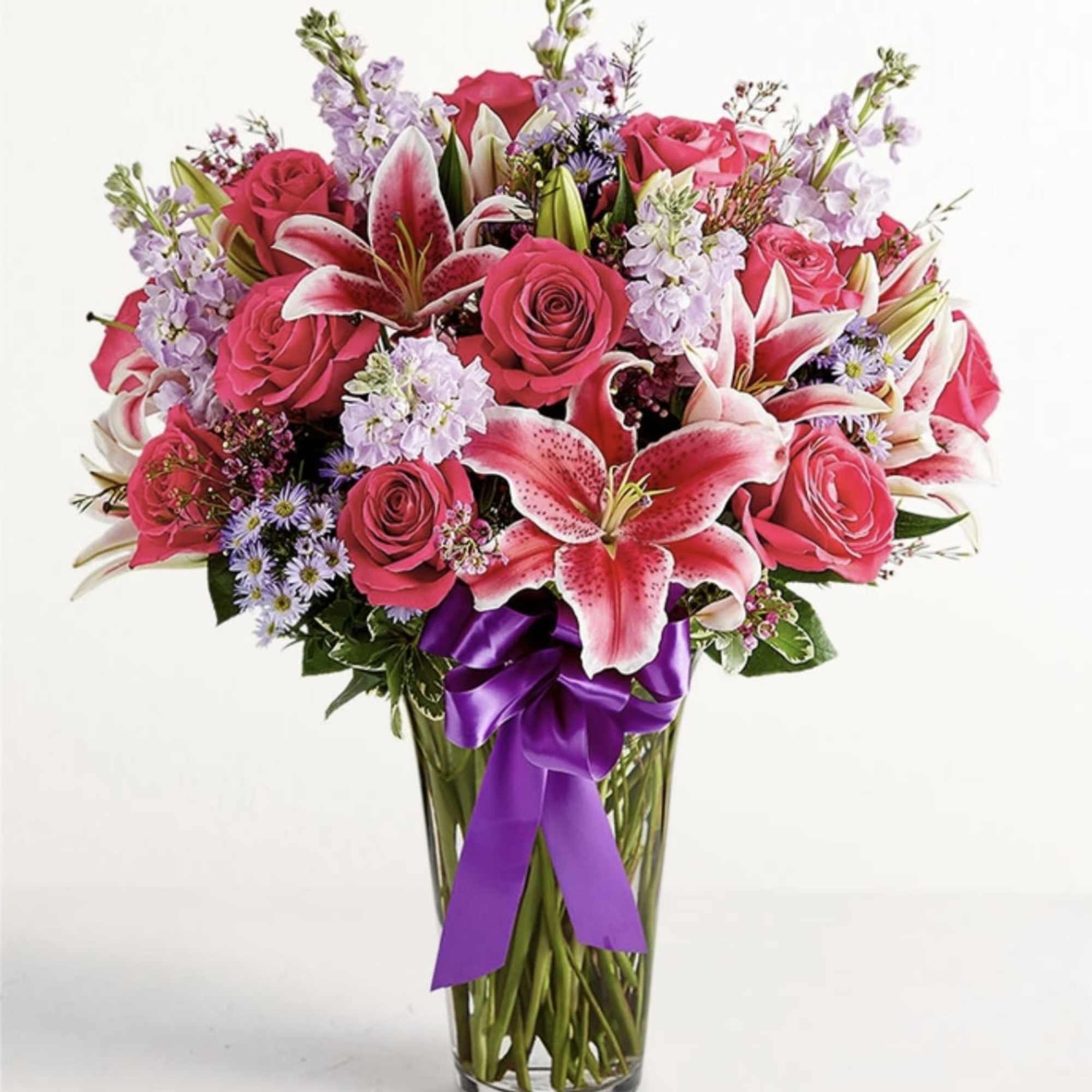 Pink roses and lilies in a clear glass vase with a purple ribbon