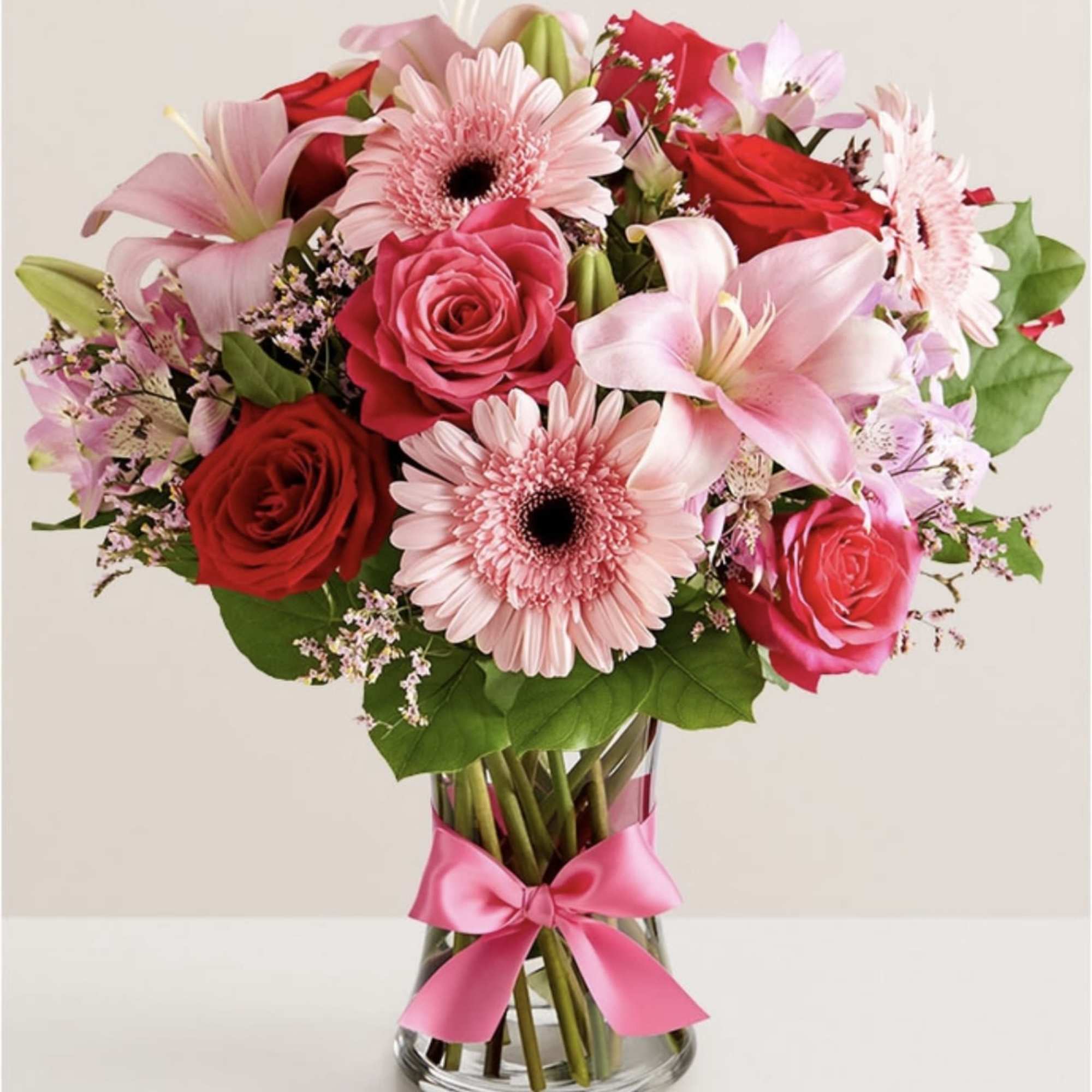 Pink and red mixed bouquet in a clear glass vase with a pink ribbon