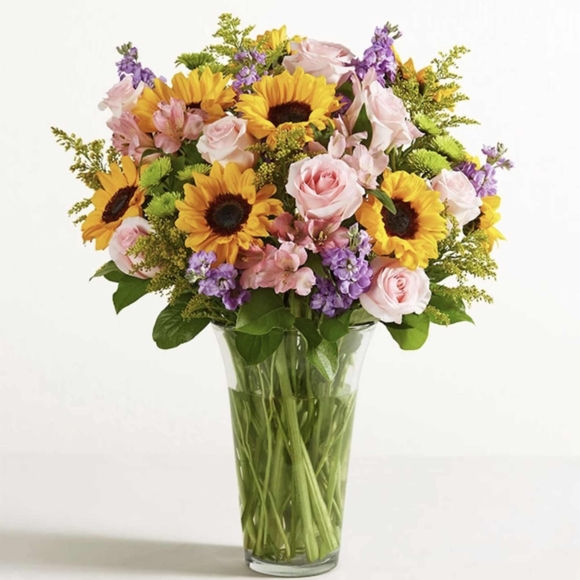 Bouquet of sunflowers, pink roses, and purple flowers in a glass vase
