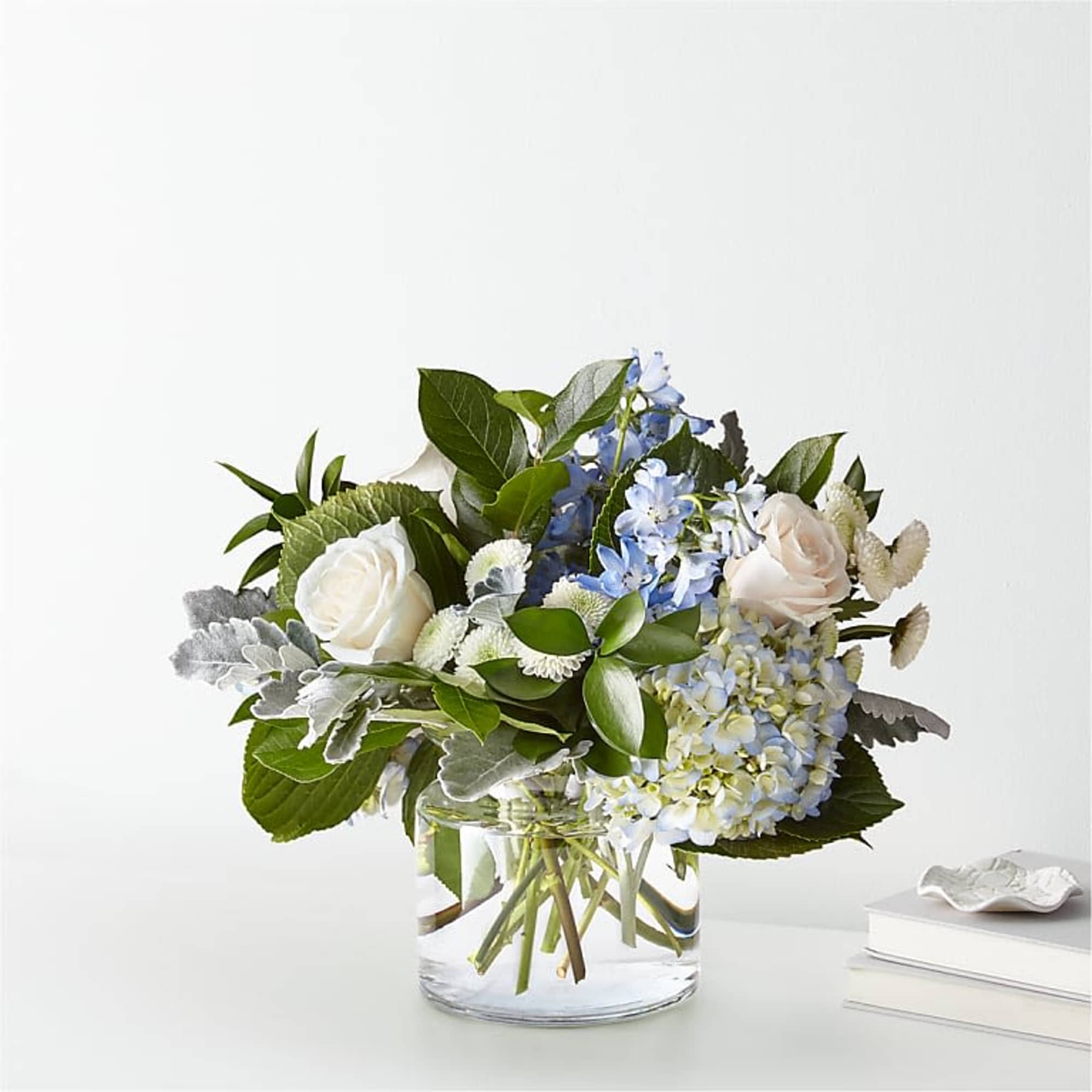 White roses and blue flowers in a clear glass vase