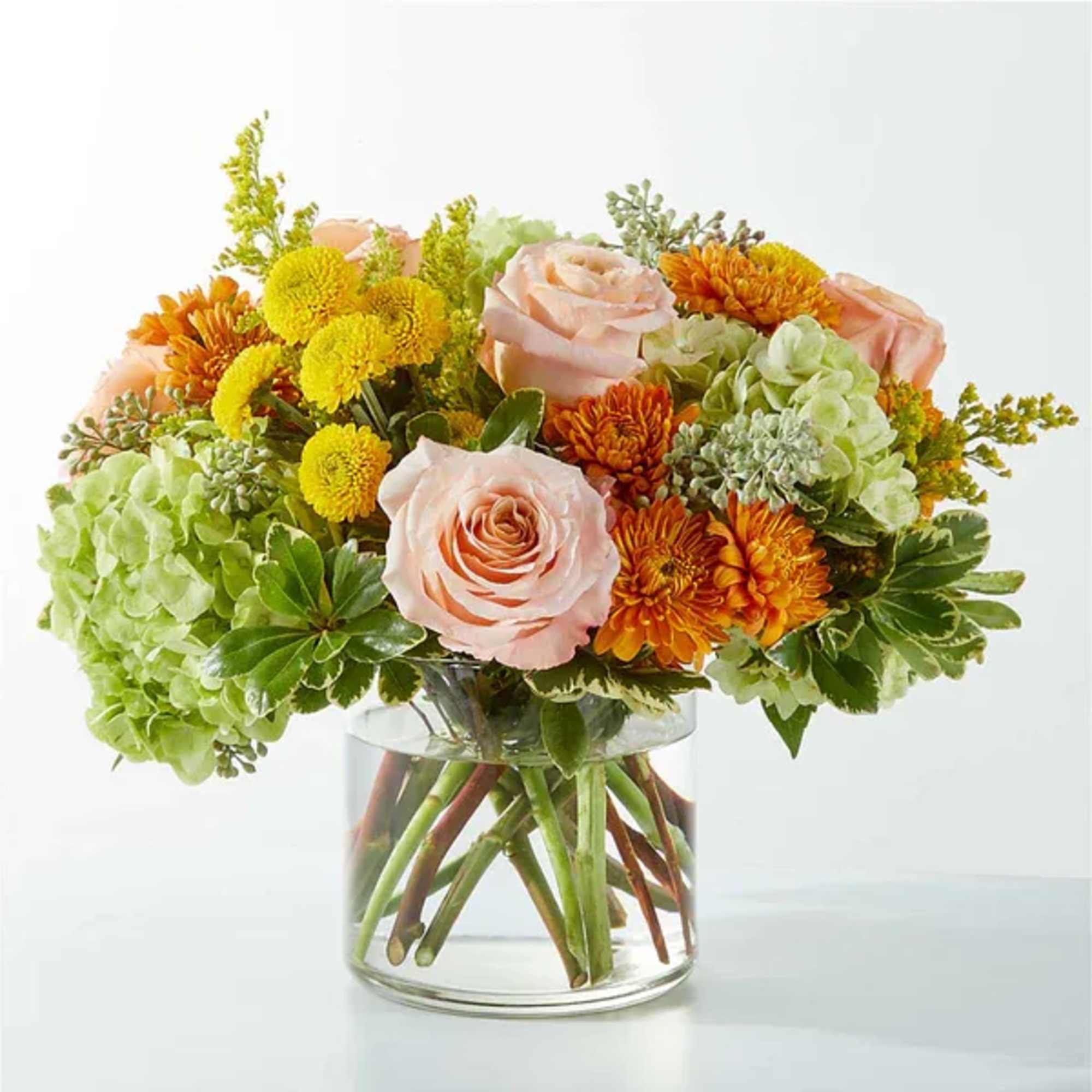 Mixed bouquet of peach roses, green hydrangeas, and orange mums in a glass vase