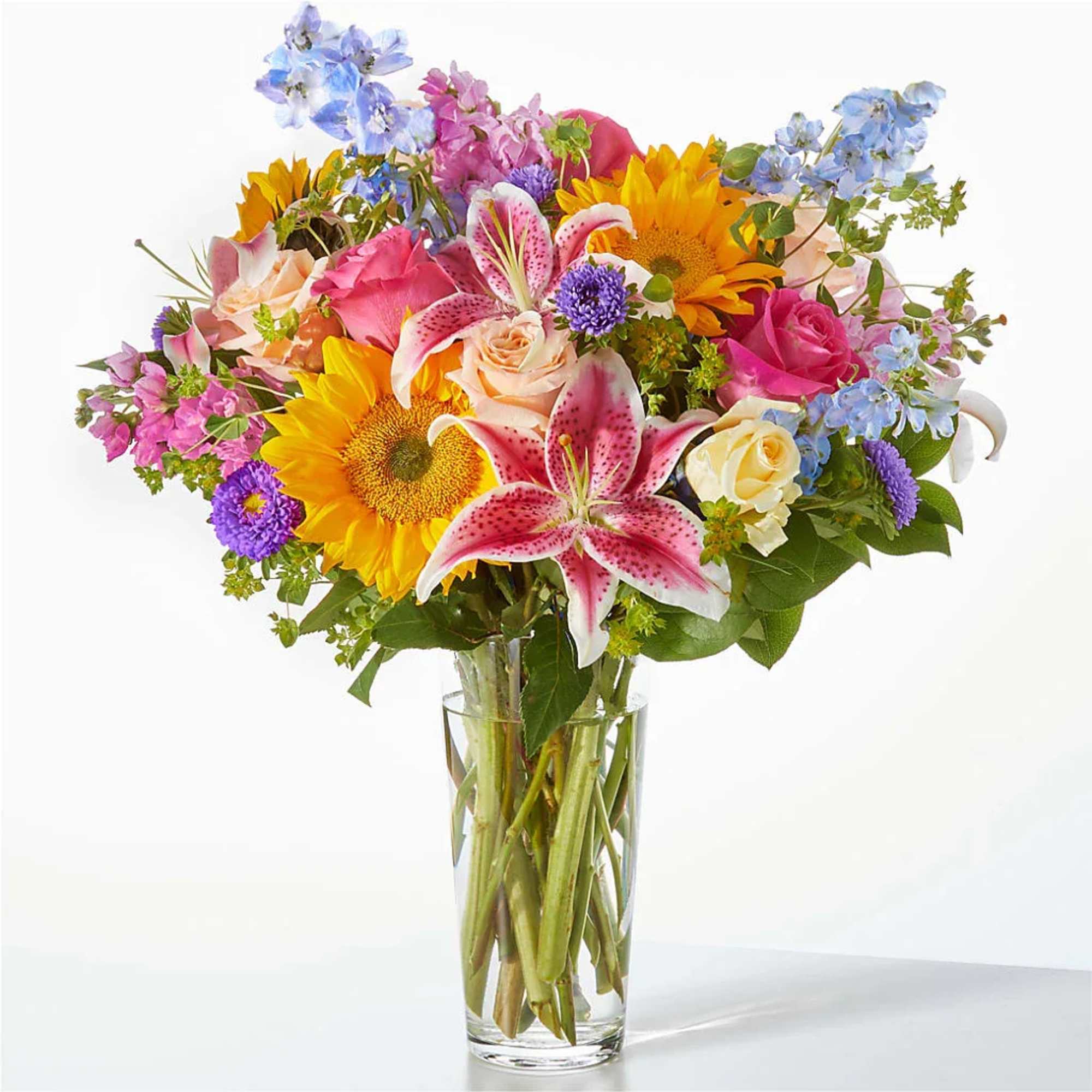 Mixed bouquet with sunflowers, lilies, and roses in a clear glass vase