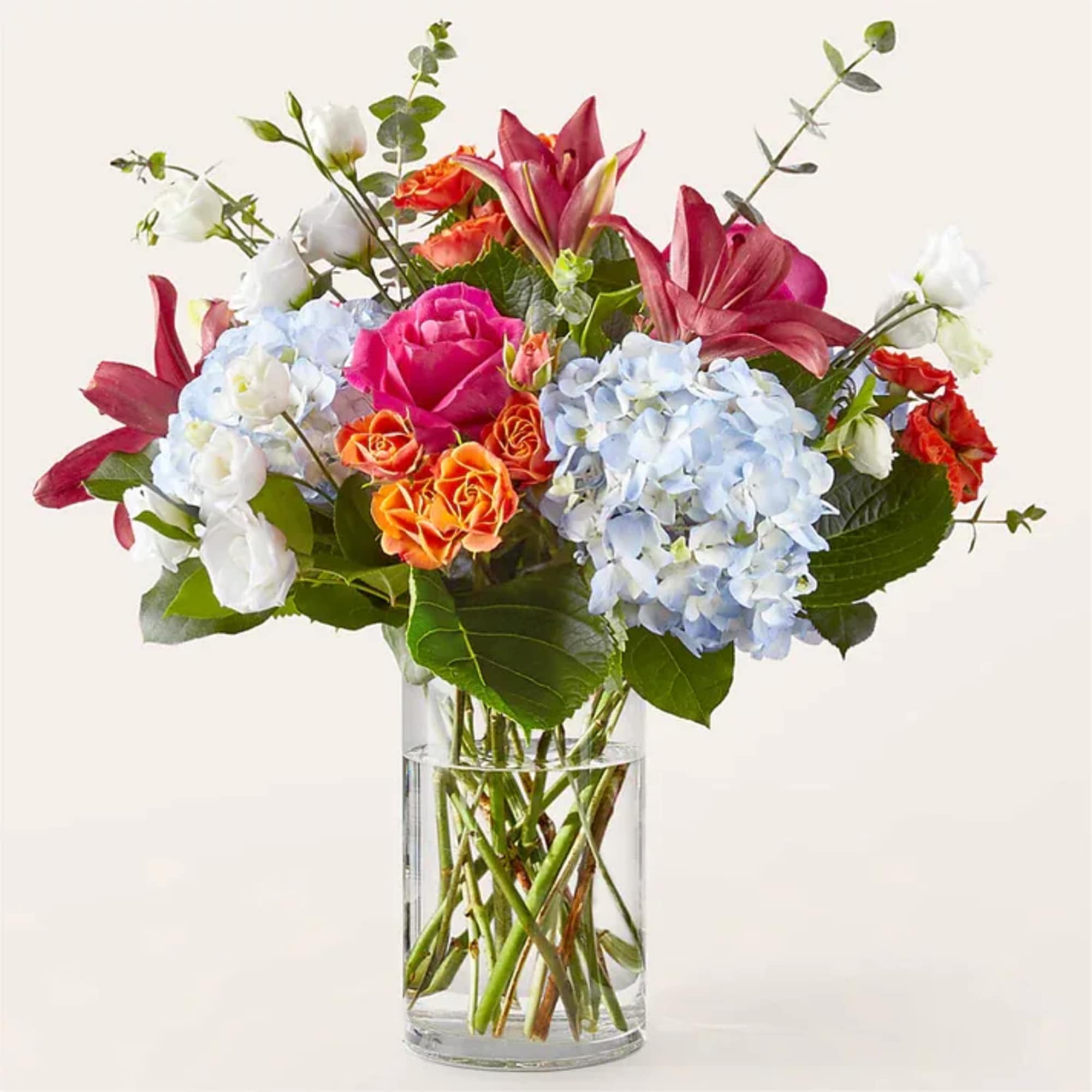 Mixed bouquet of roses, lilies, and hydrangeas in a clear glass vase