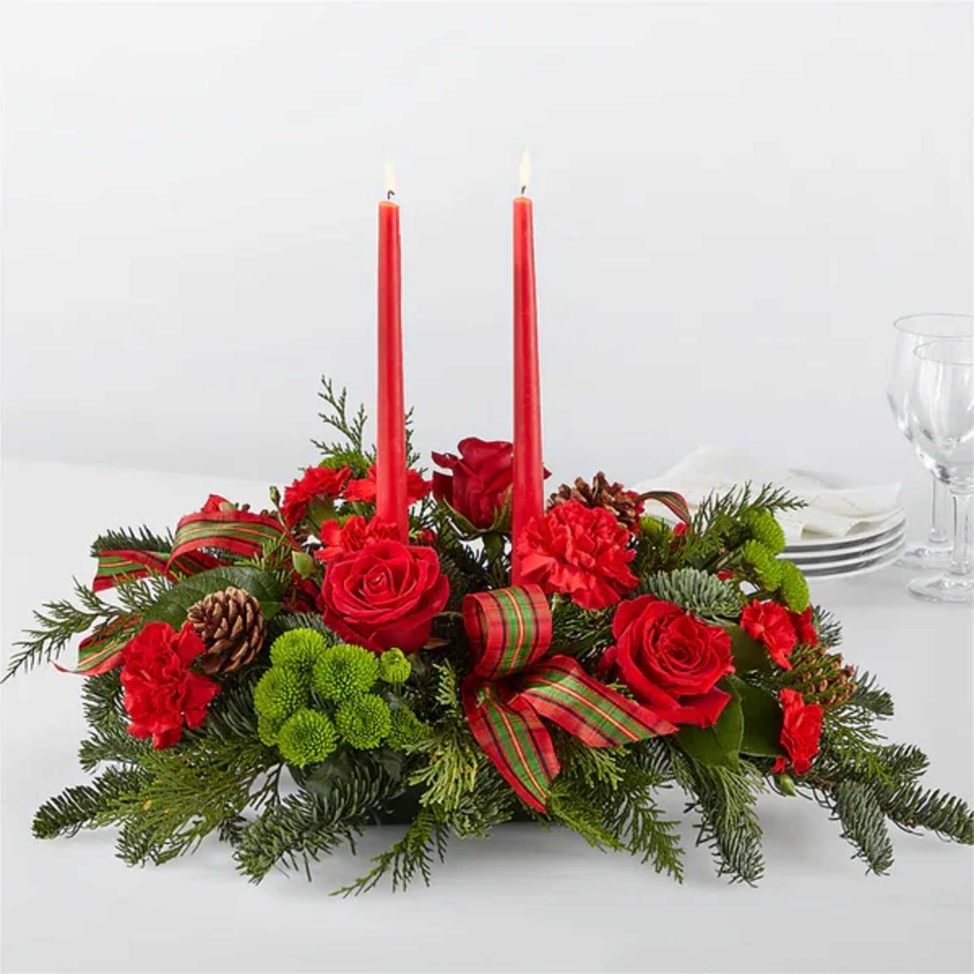 Red floral centerpiece with two lit candles and ribbon on a table