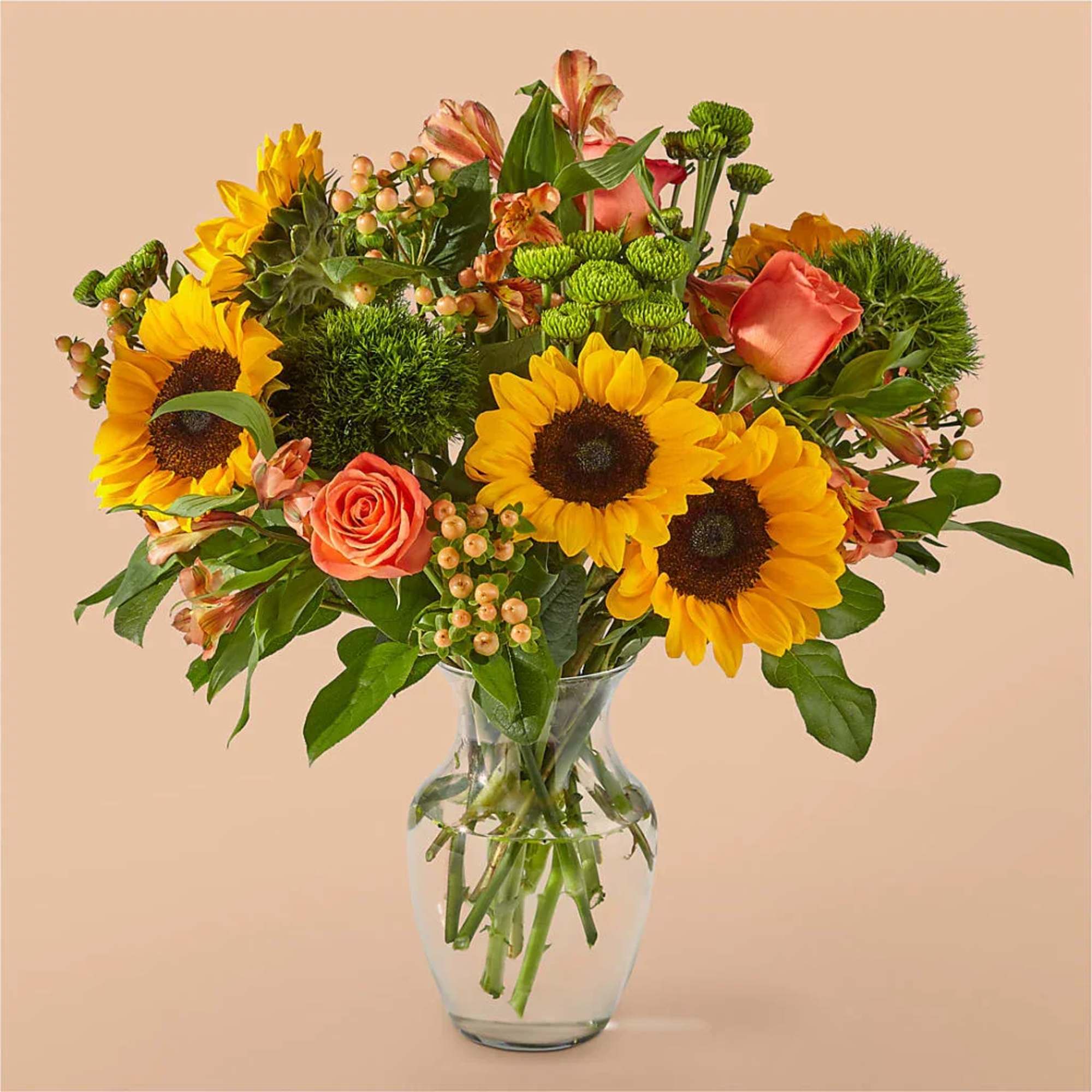 Bouquet of sunflowers and coral roses in a clear glass vase