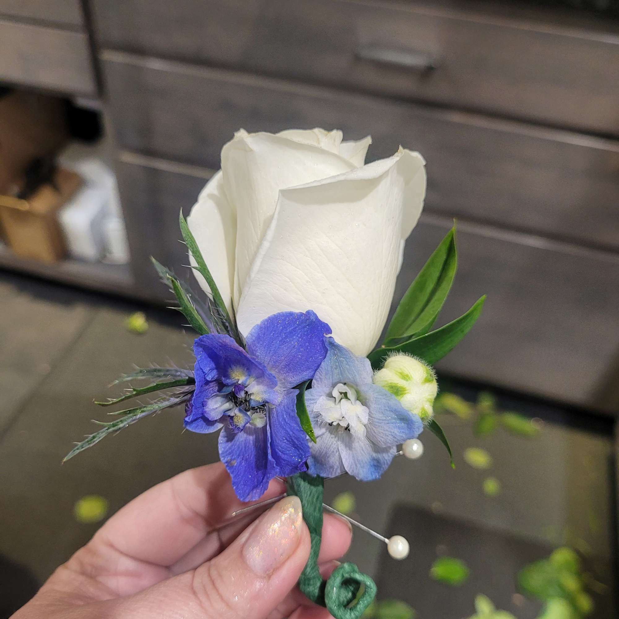 White rose boutonniere with blue flowers and green accents