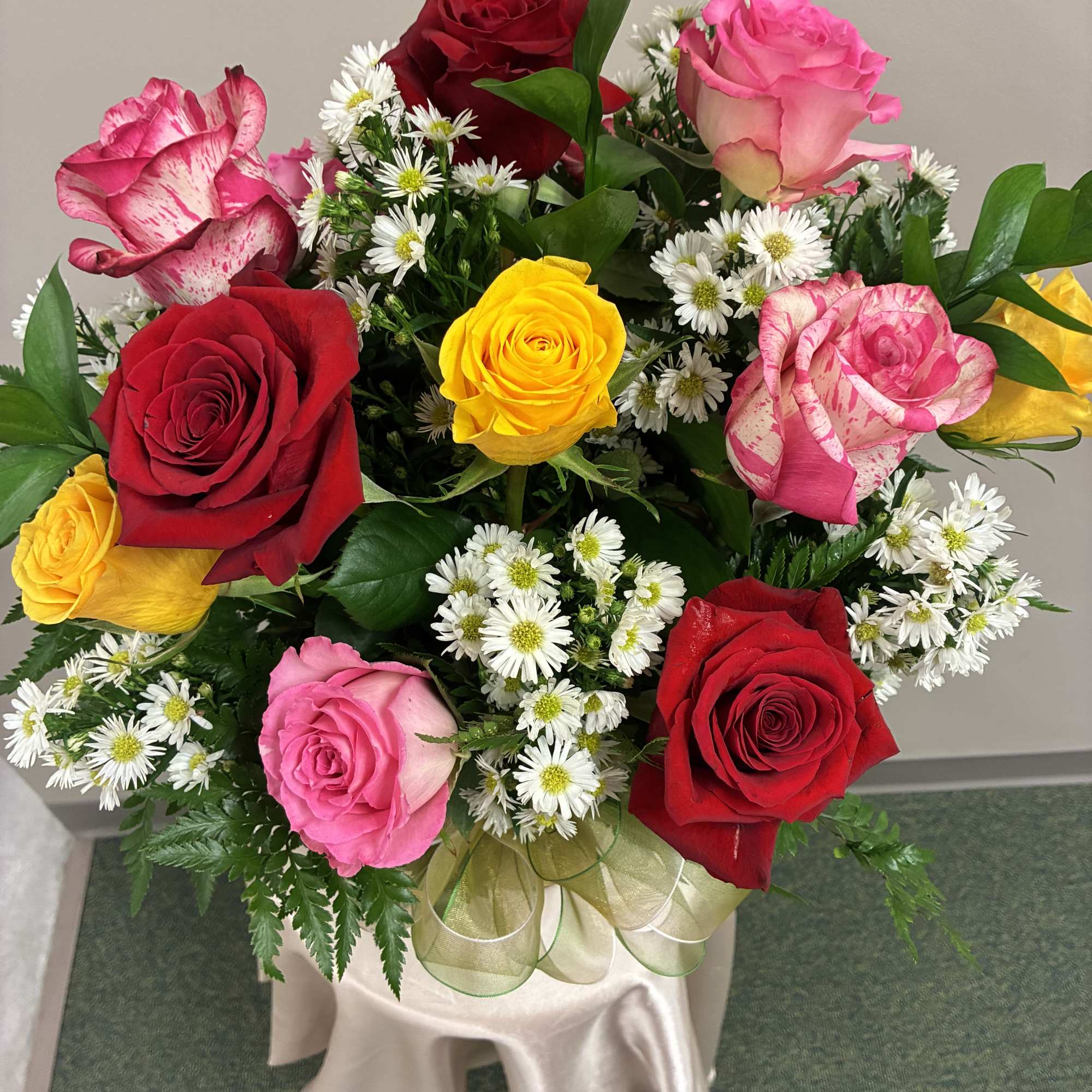 Mixed bouquet of red, pink, and yellow roses with white daisies in a vase