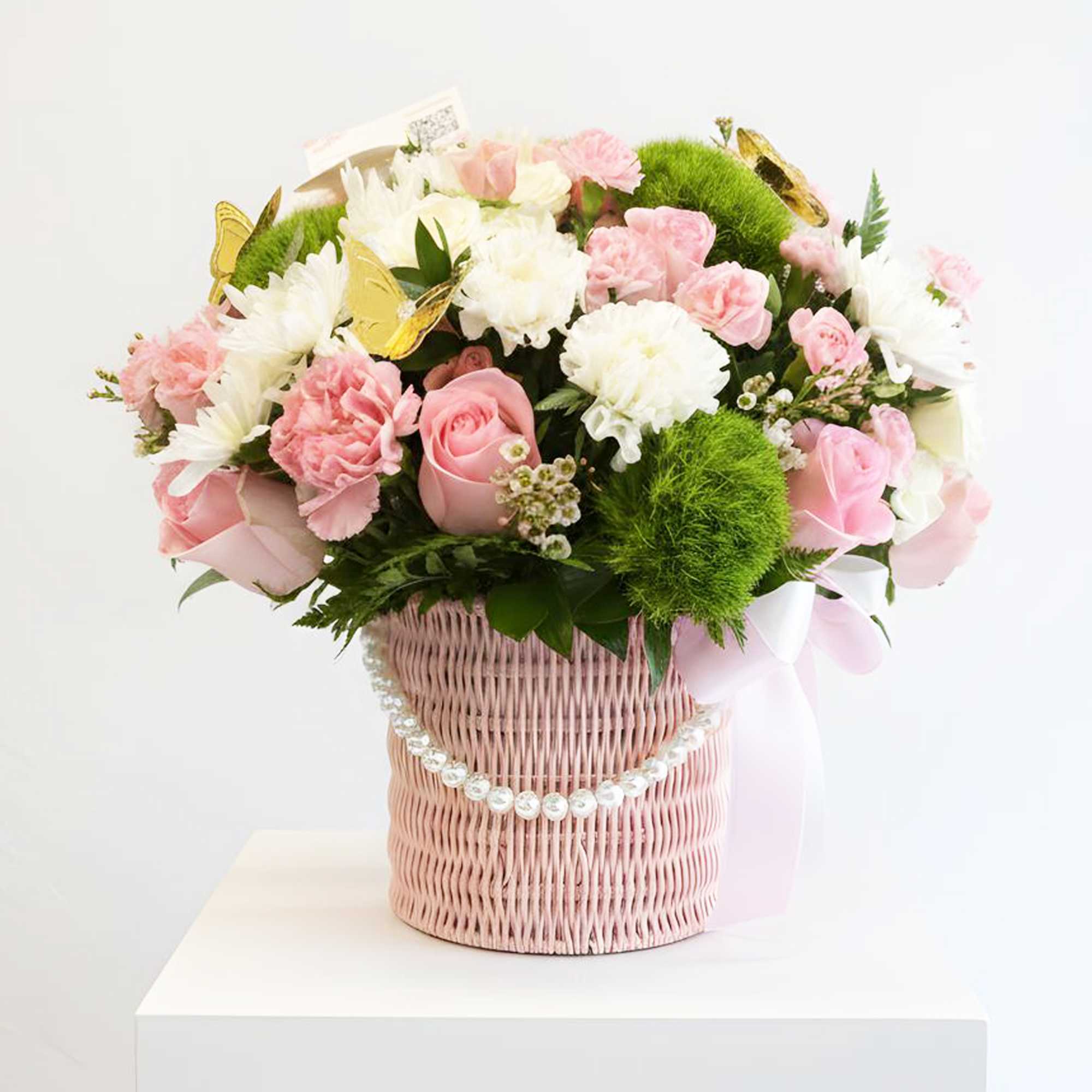 Pink and white flower arrangement in a pink wicker basket with butterfly accents