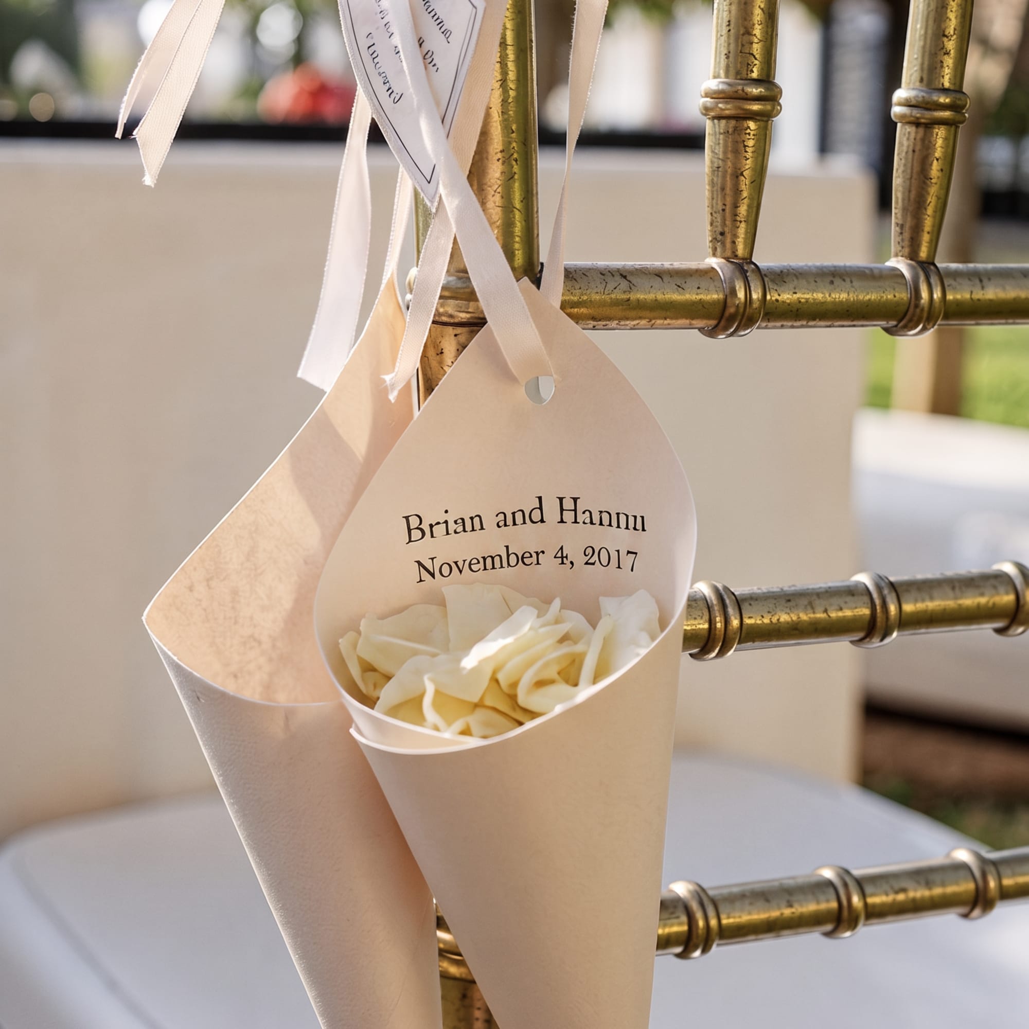 Cream rose petals in paper cones tied to a gold chair