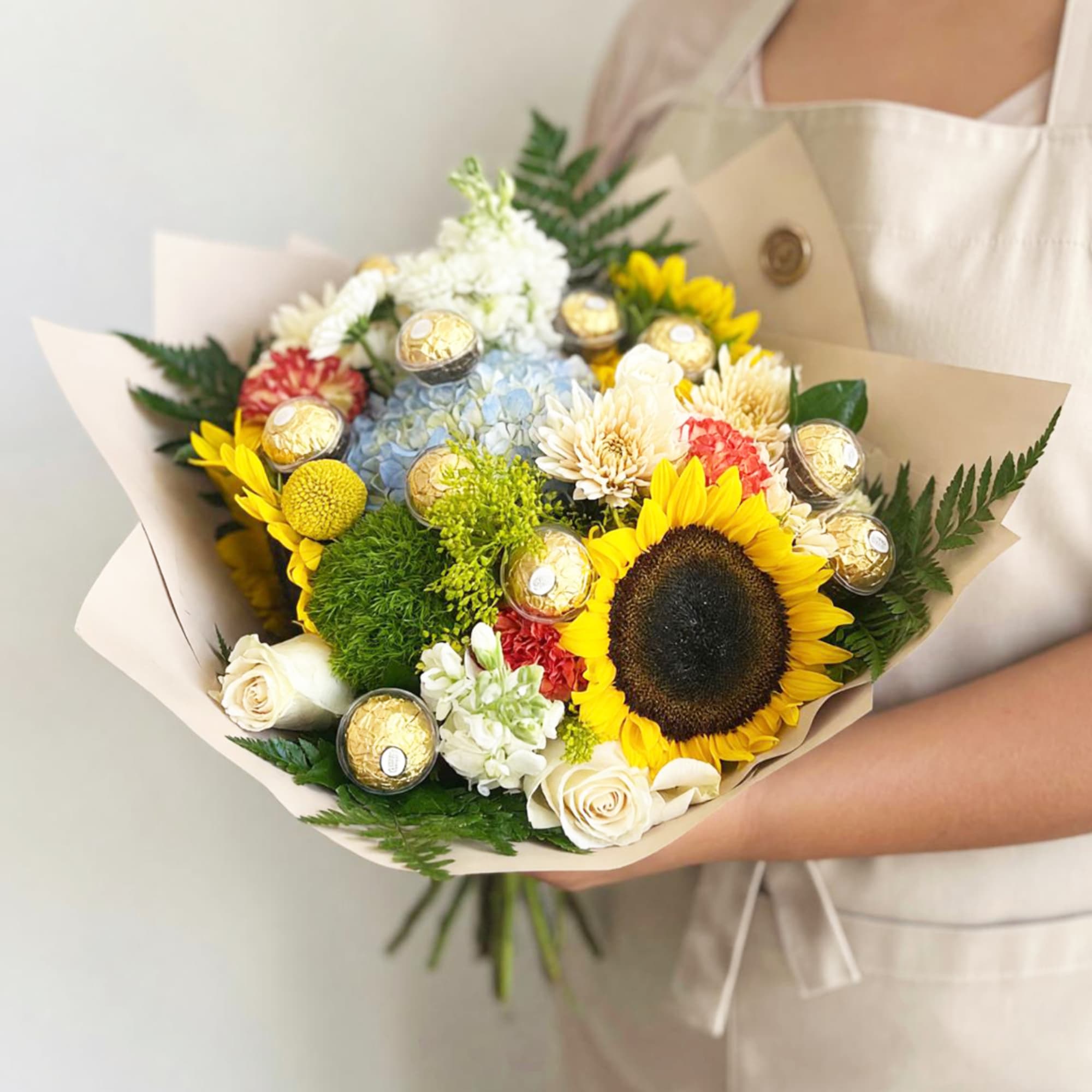Handheld bouquet with a sunflower, roses, hydrangea, and chocolates