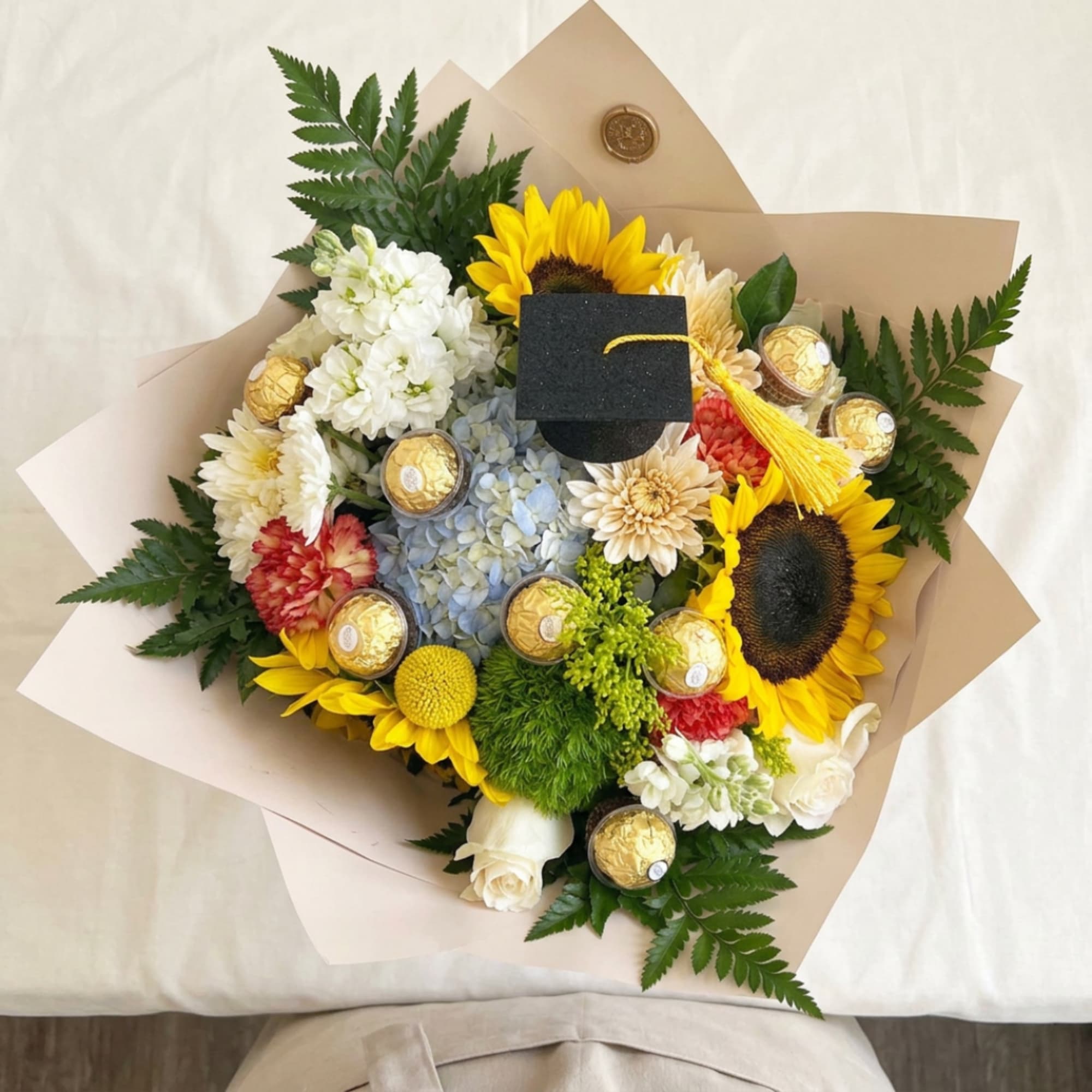 Bouquet with sunflowers, white blooms, and chocolates wrapped in tan paper