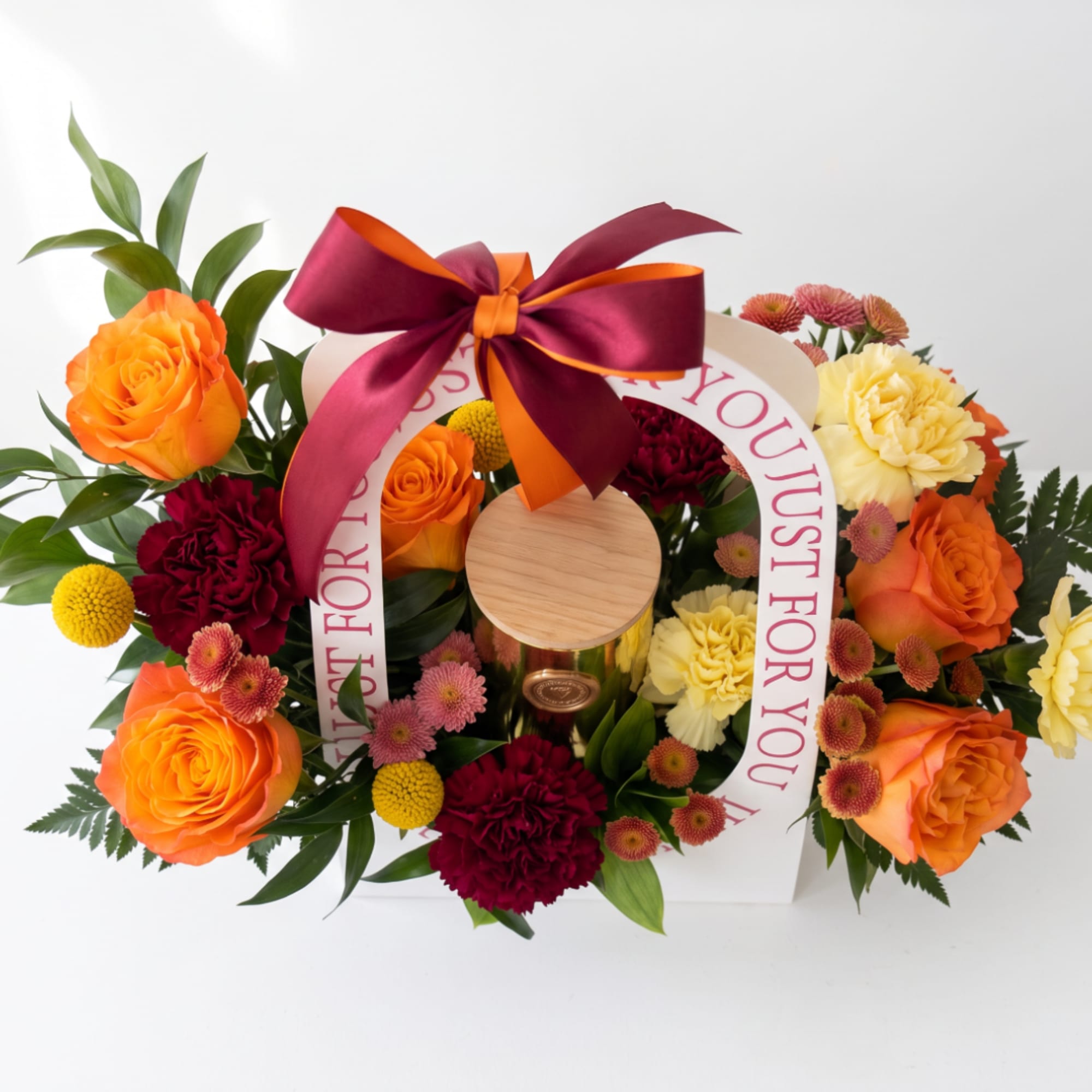 Orange roses and mixed flowers arranged around a gift box with a ribbon bow