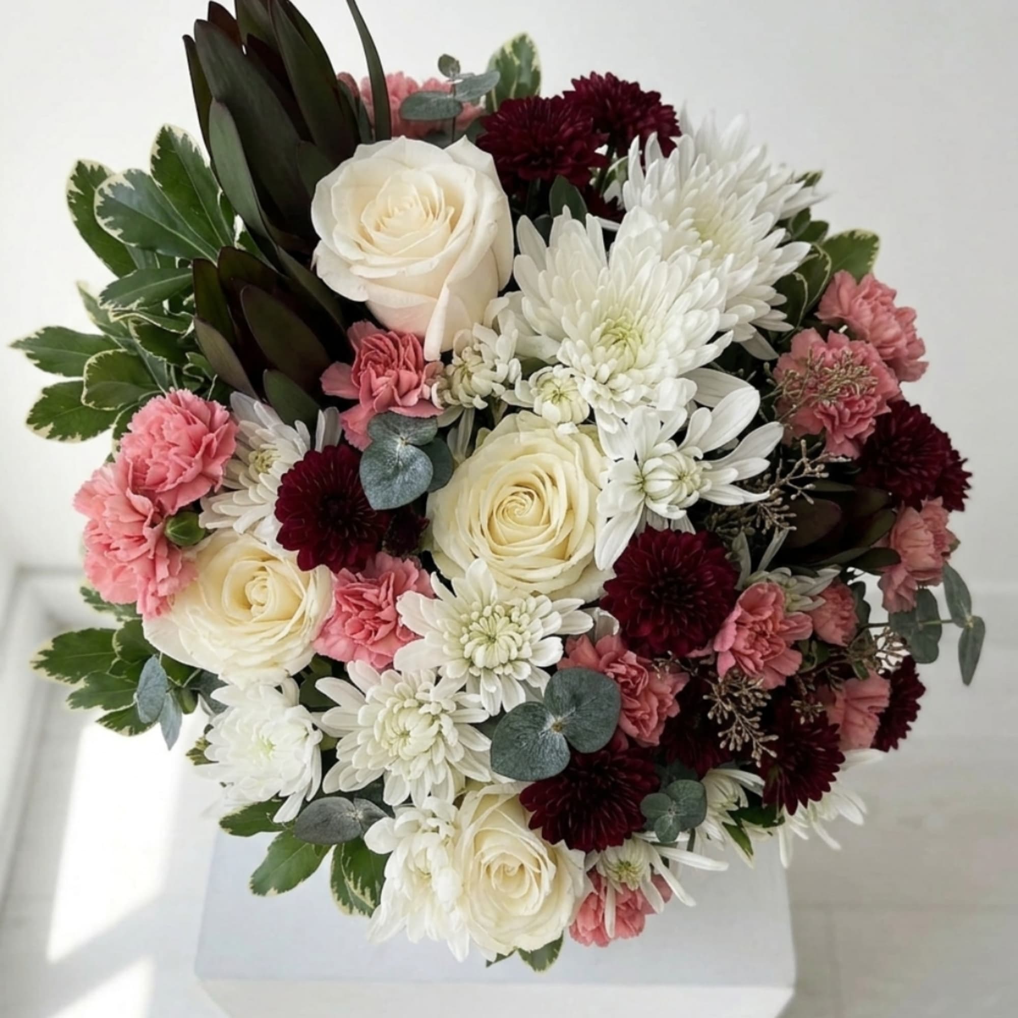 Round bouquet of white roses, white chrysanthemums, pink carnations, and burgundy blooms