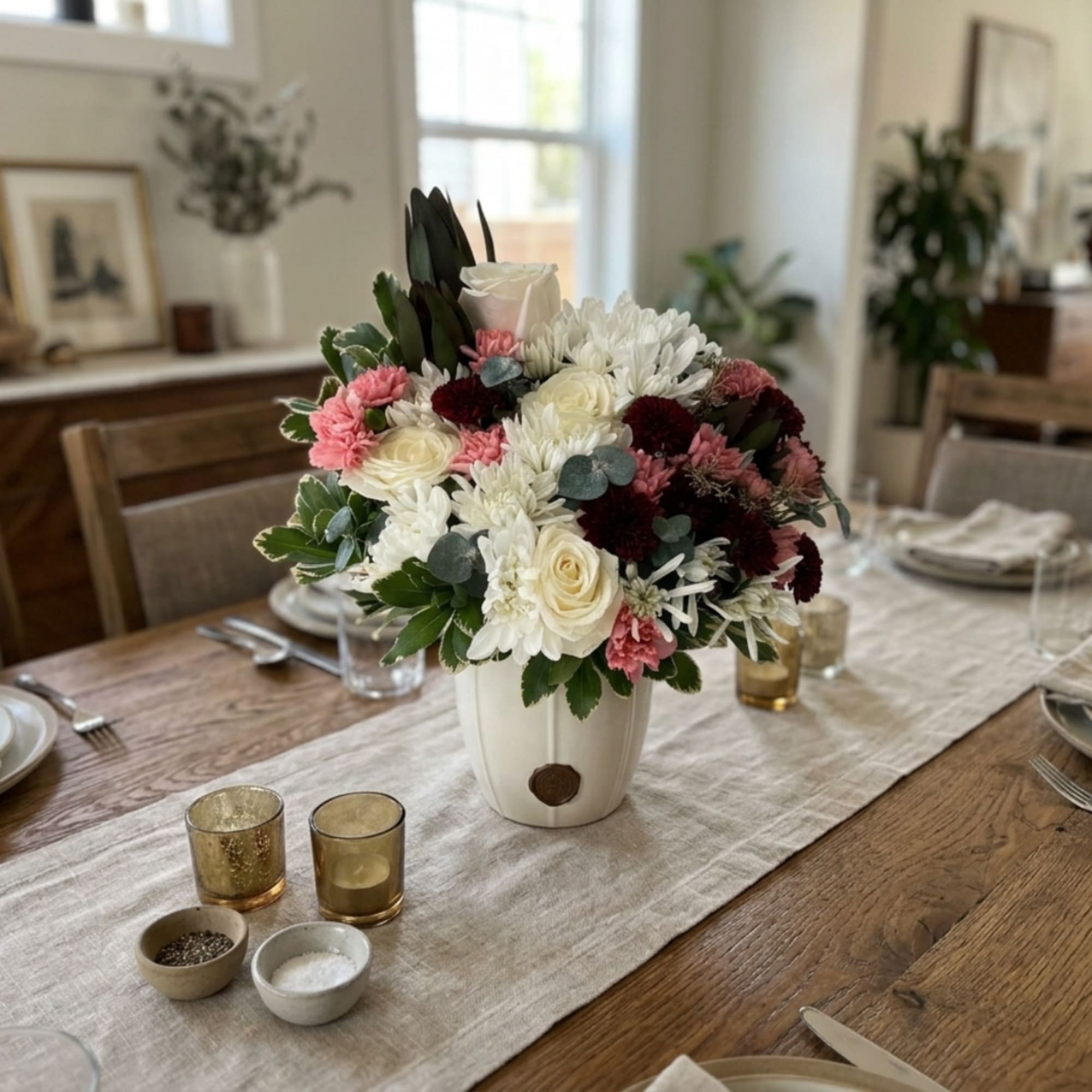 Mixed white, pink, and burgundy flowers arranged in a white vase on a dining table