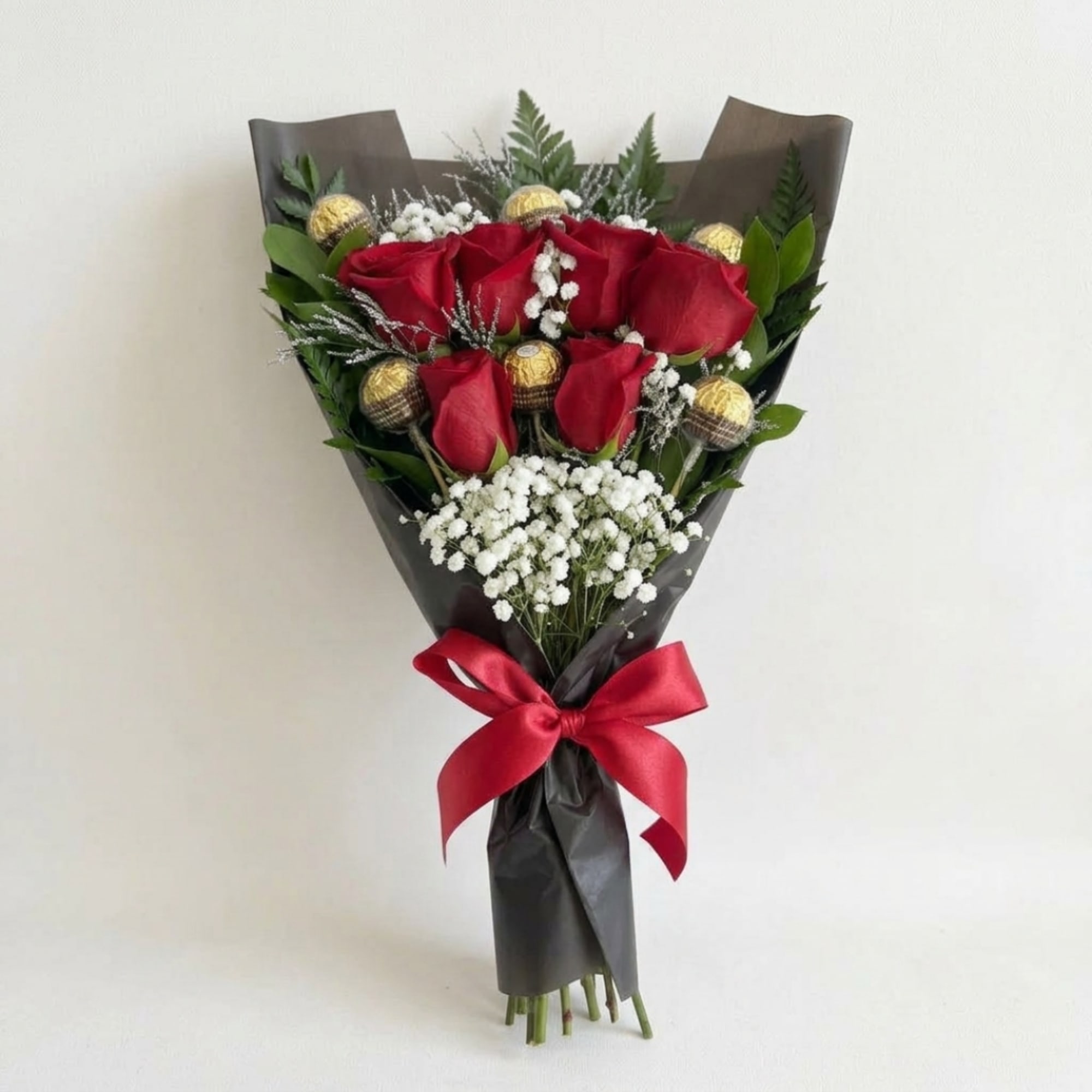 Bouquet of red roses with white filler flowers, wrapped in black paper and tied with a red ribbon