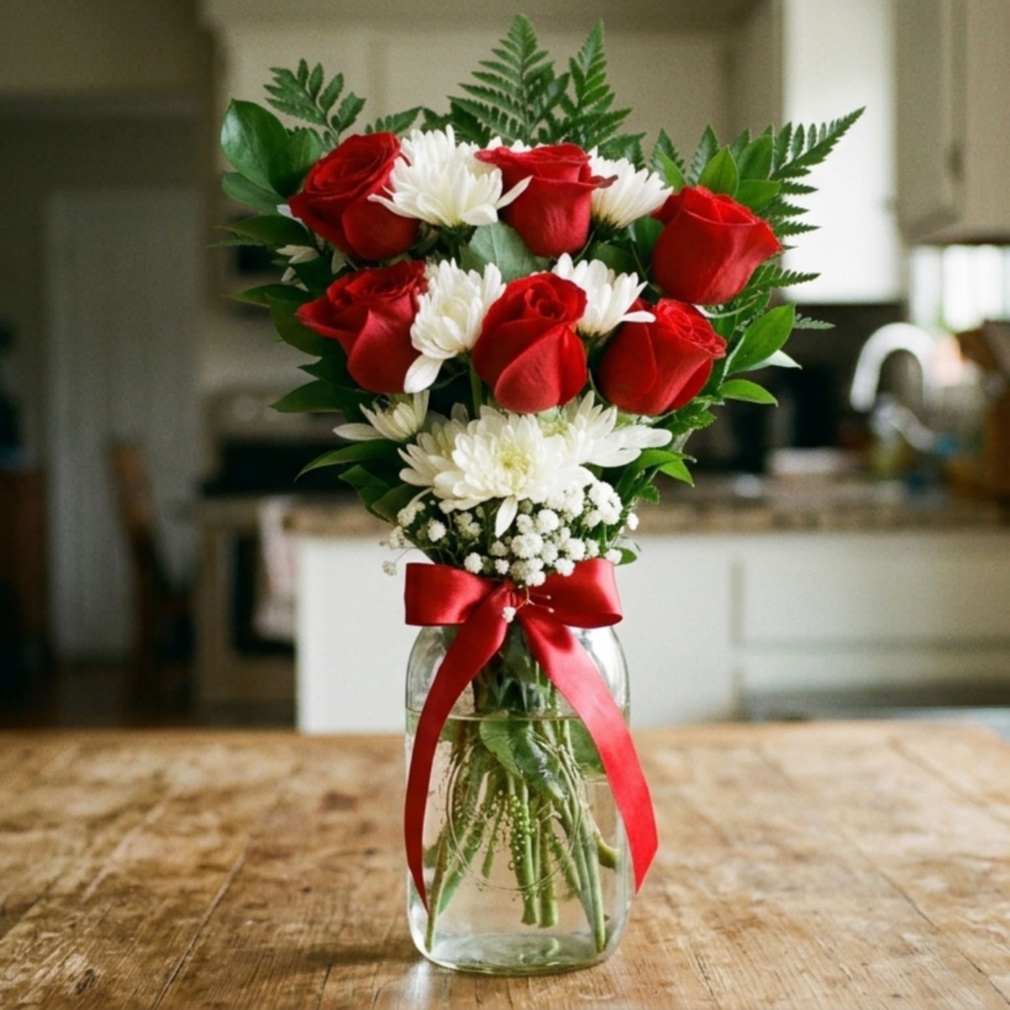 Red roses and white daisies in a glass jar with a red ribbon