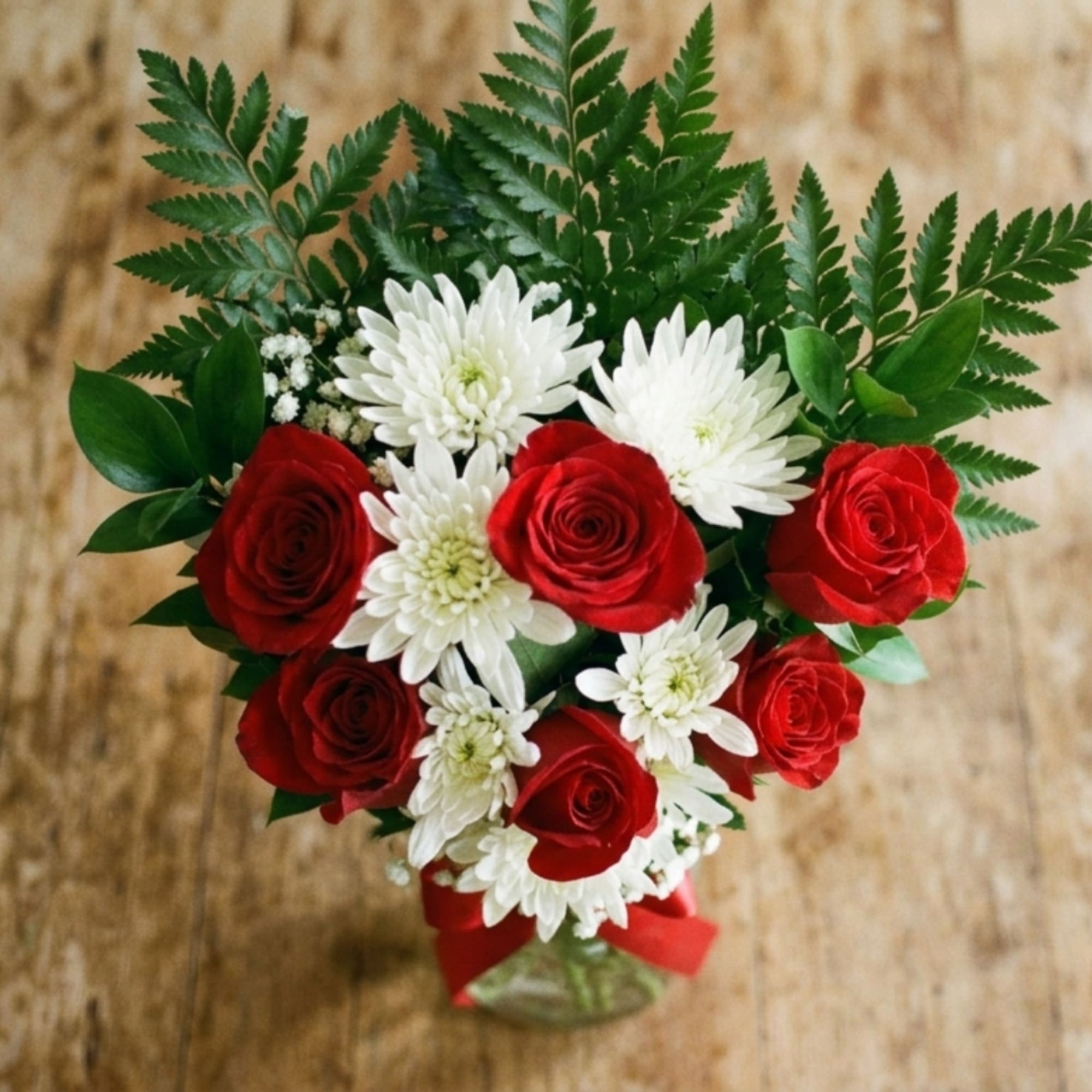 Bouquet of red roses and white daisies with greenery in a vase