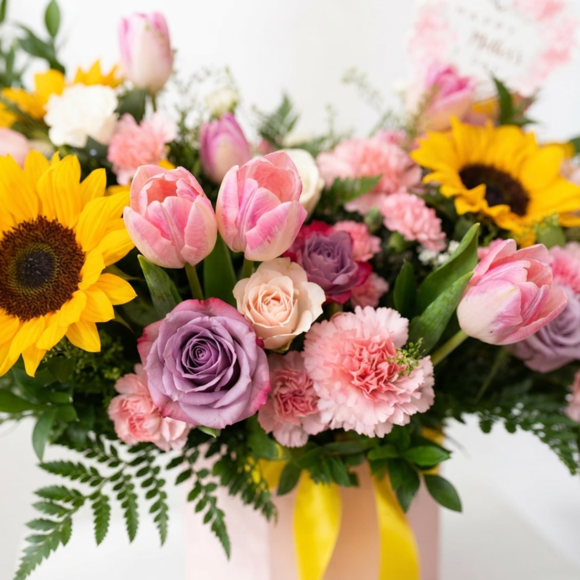 Mixed bouquet with pink tulips, sunflowers, roses, and carnations in a pink box