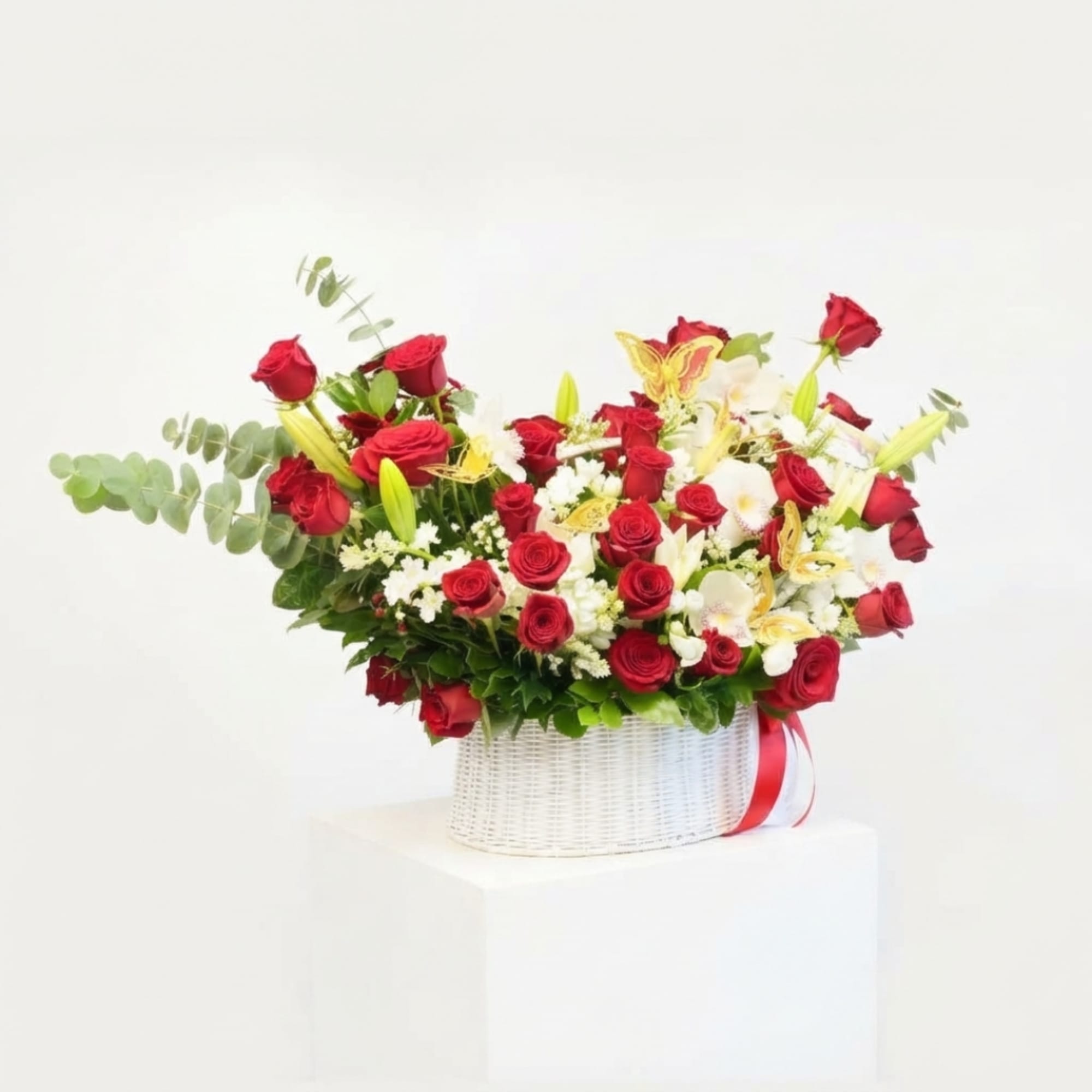 Red roses and white lilies arranged in a white basket with a red ribbon