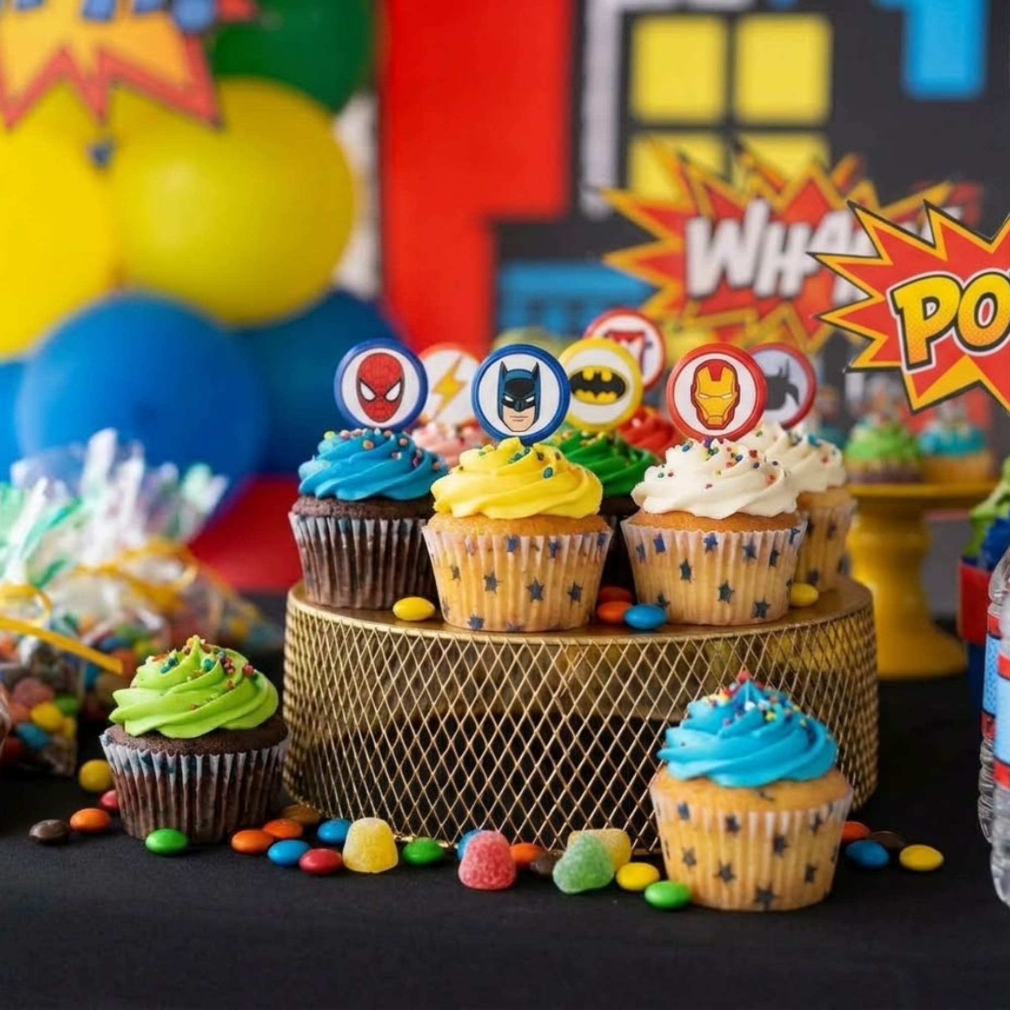 Superhero-themed cupcakes on a stand with colorful frosting and toppers